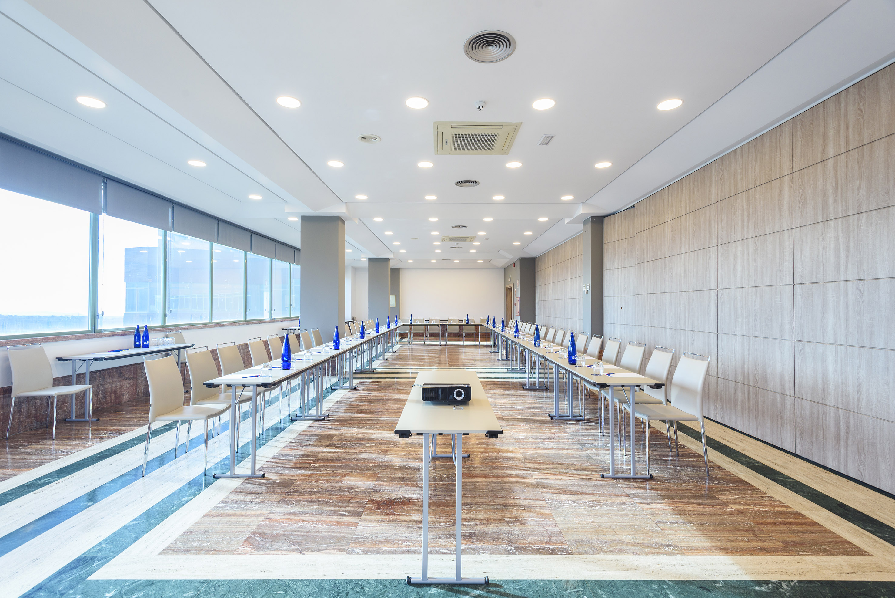 Modern U-shaped conference room with projector, tables, chairs, and large windows.