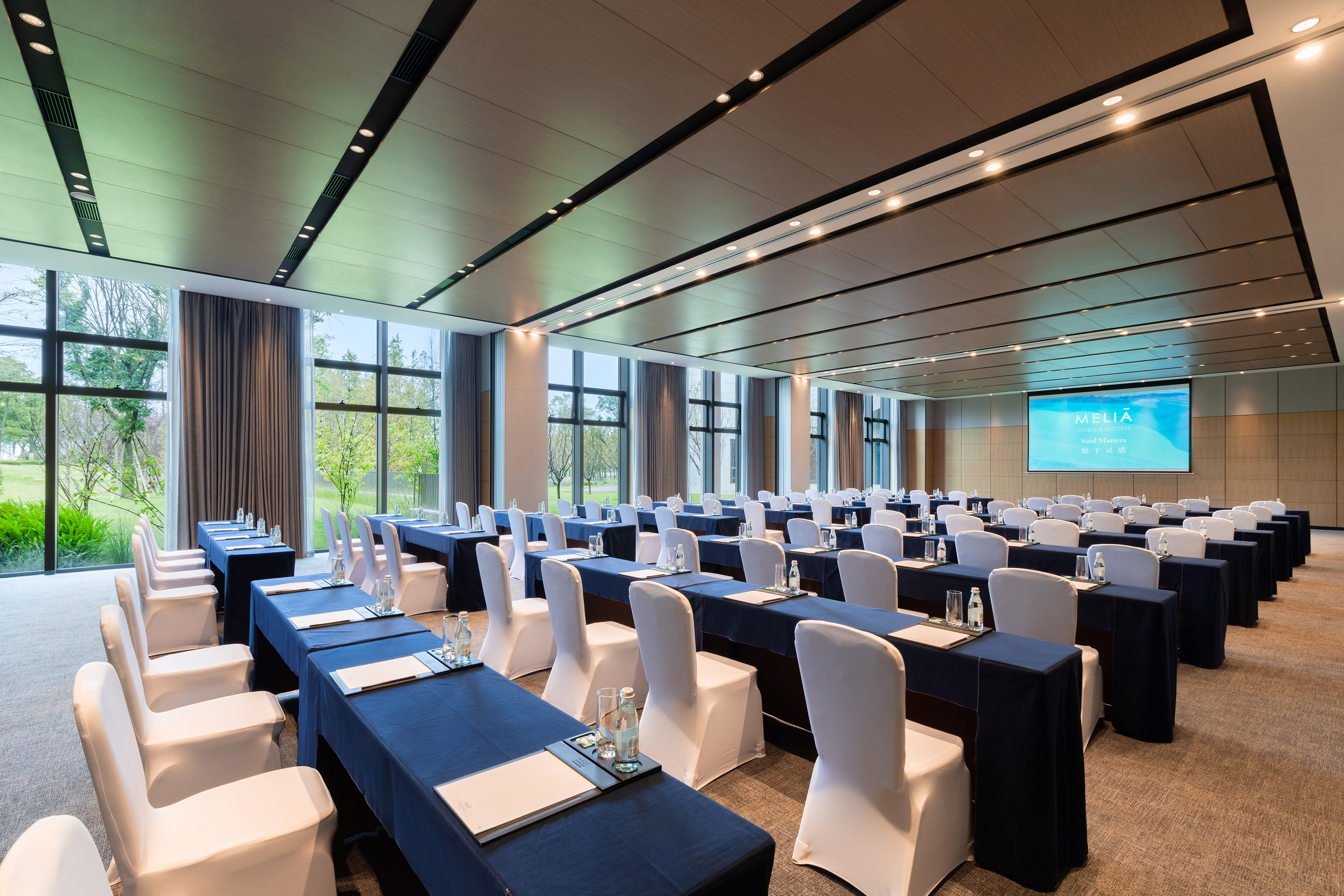 Bright Melia conference room with blue tables, white chairs, and projector.