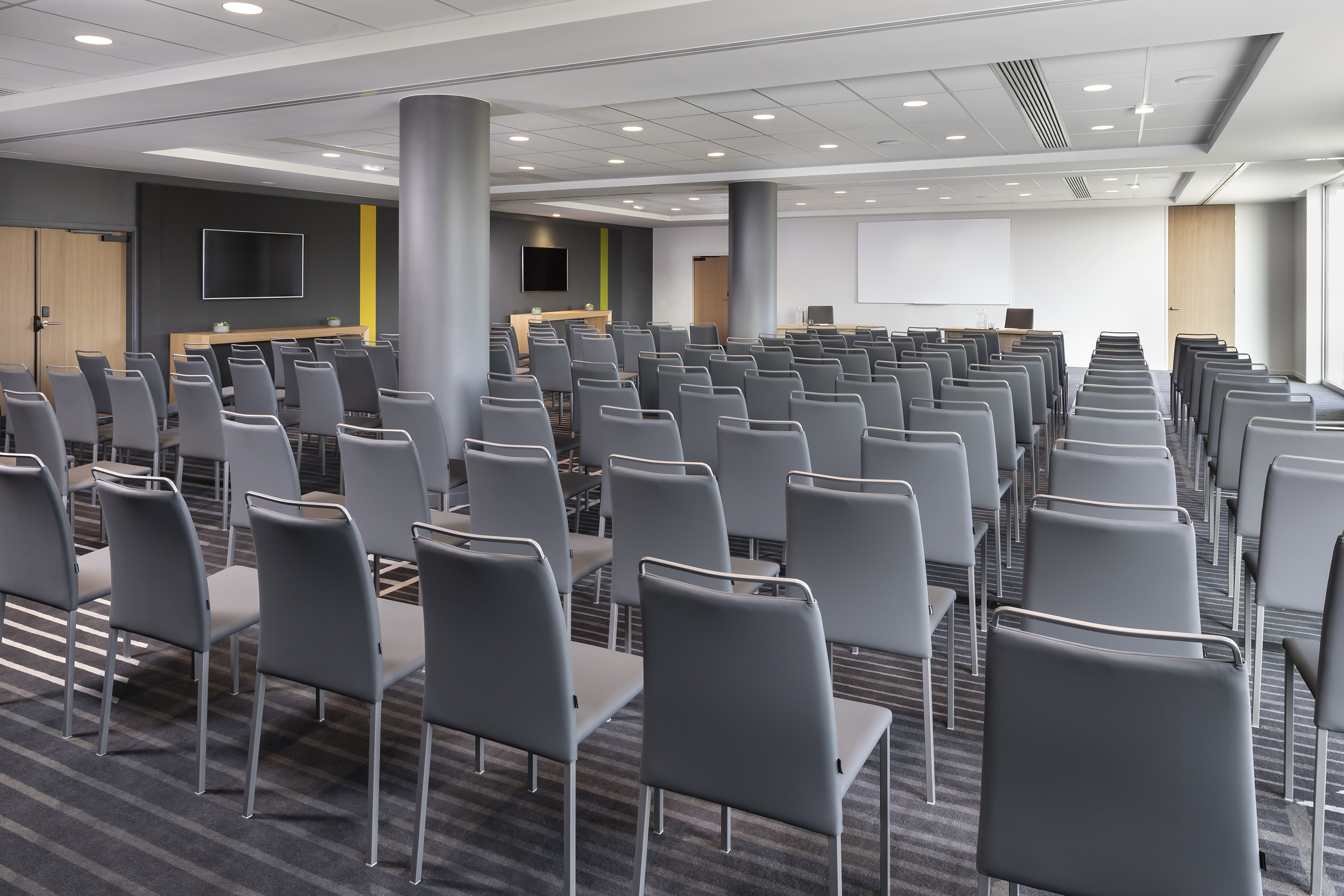 Modern conference room setup with grey chairs, large TV, and presentation screen.