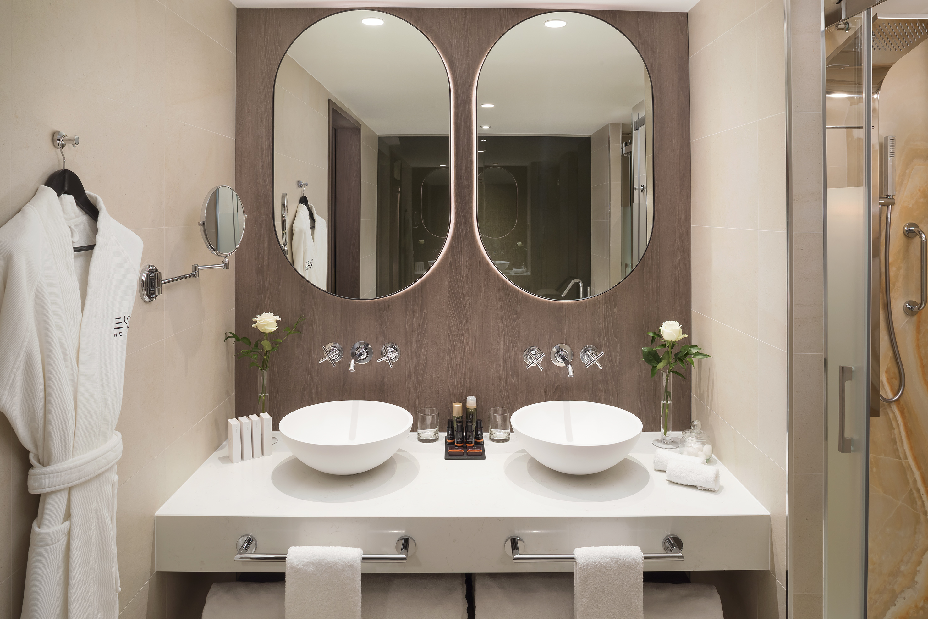 Luxury hotel bathroom with double vanity, vessel sinks, and backlit mirrors.
