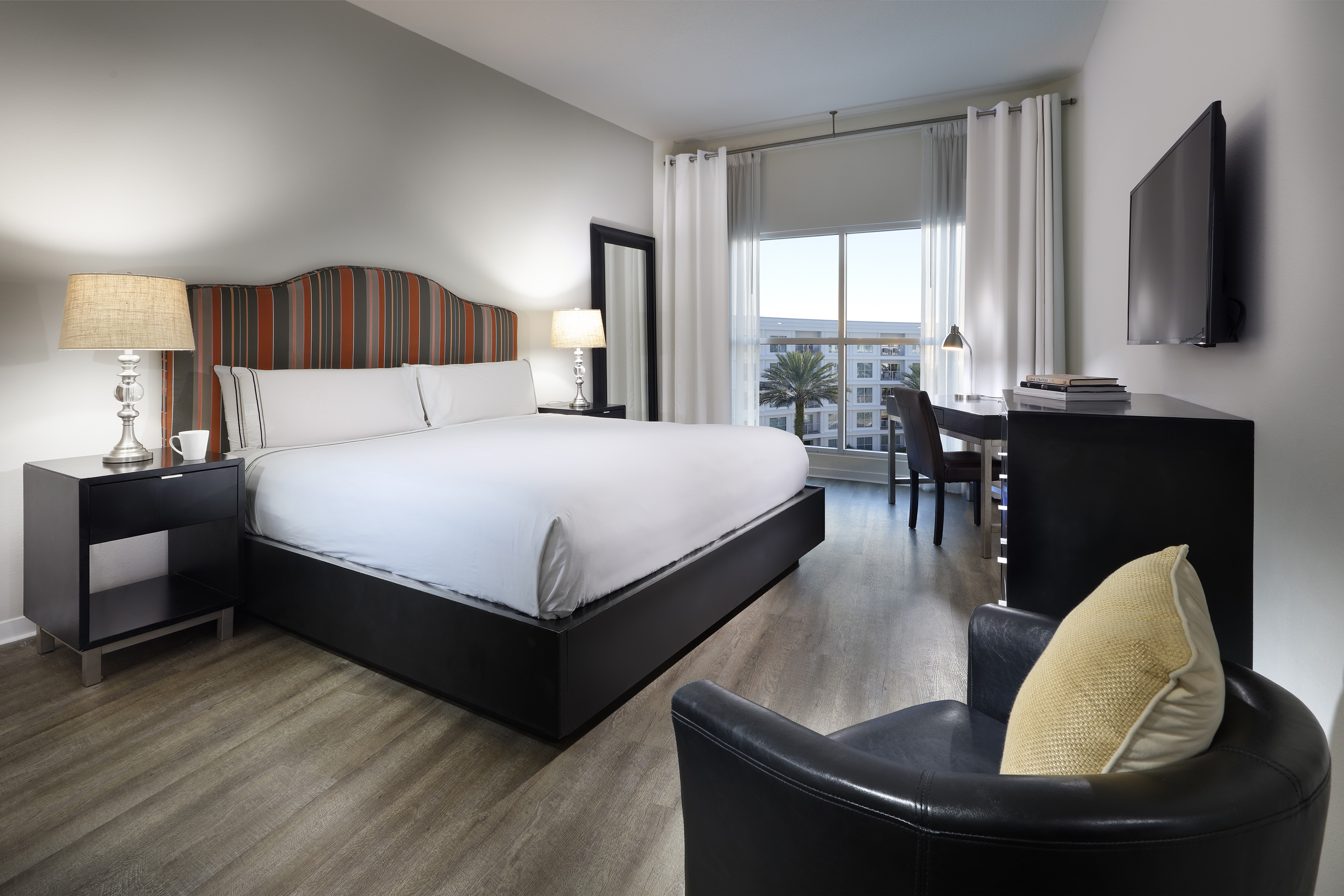 Modern hotel bedroom with king bed, striped headboard, desk, TV, and city view. - Two-Bedroom Family Suite - Meliá Orlando Celebration, Orlando