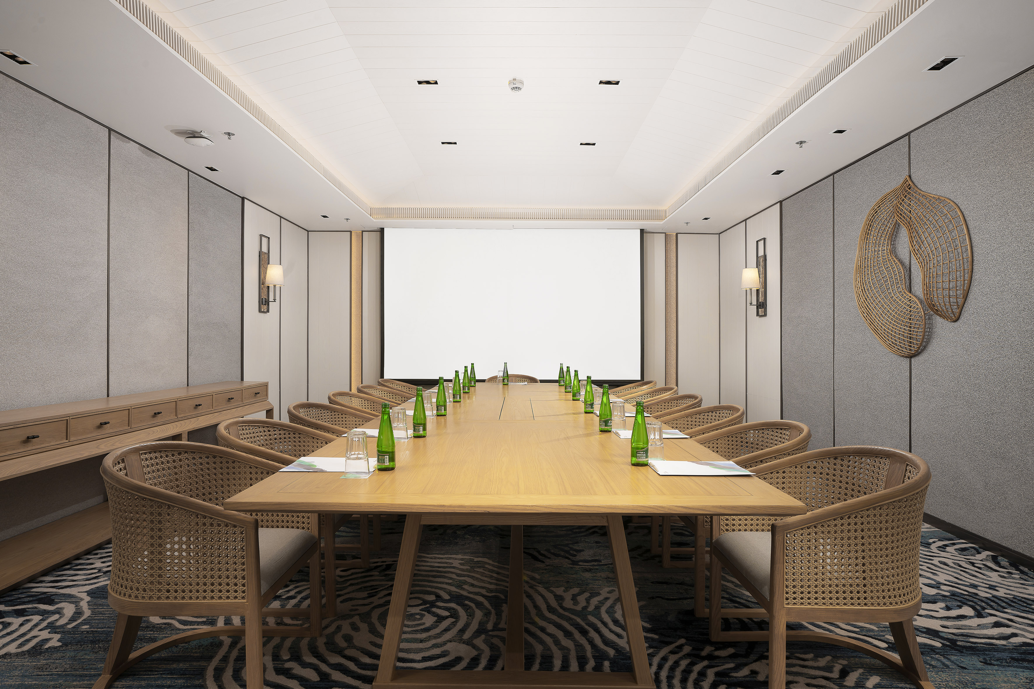 Modern meeting room with wooden table, rattan chairs, and projector screen.