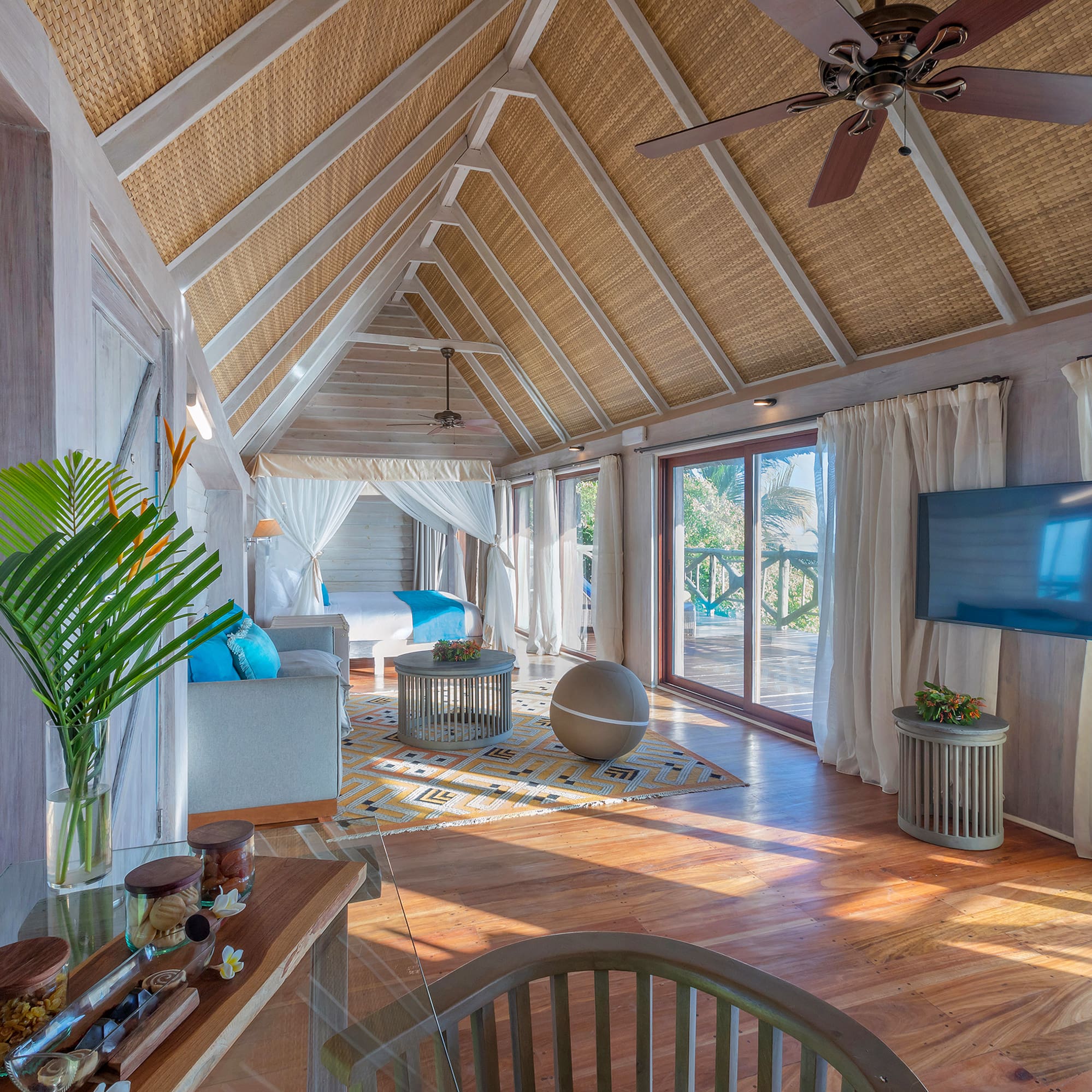 Spacious tropical resort suite with vaulted rattan ceiling, bed, and balcony.