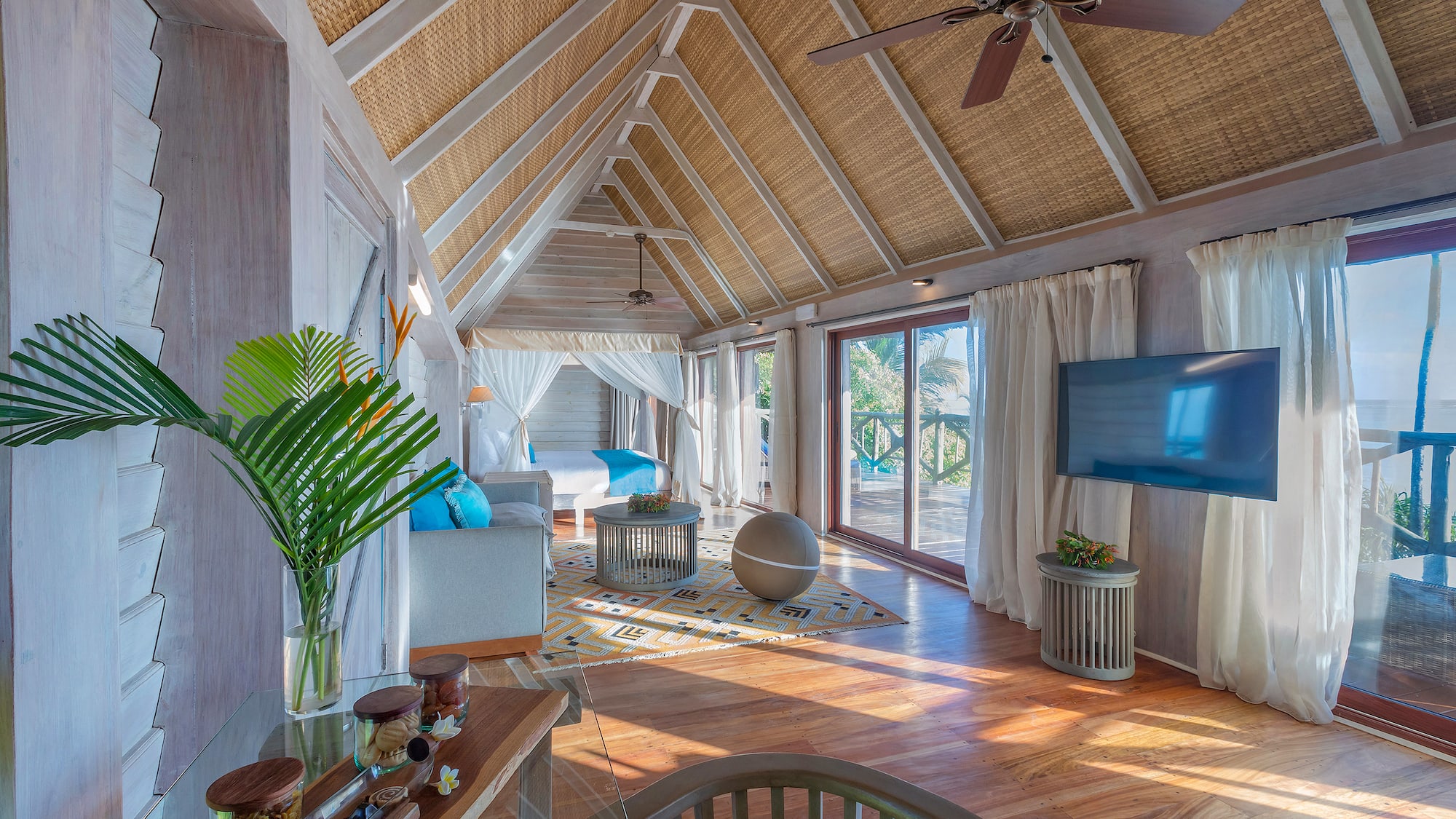 Luxurious tropical suite with vaulted woven ceiling, wooden floor, and balcony.
