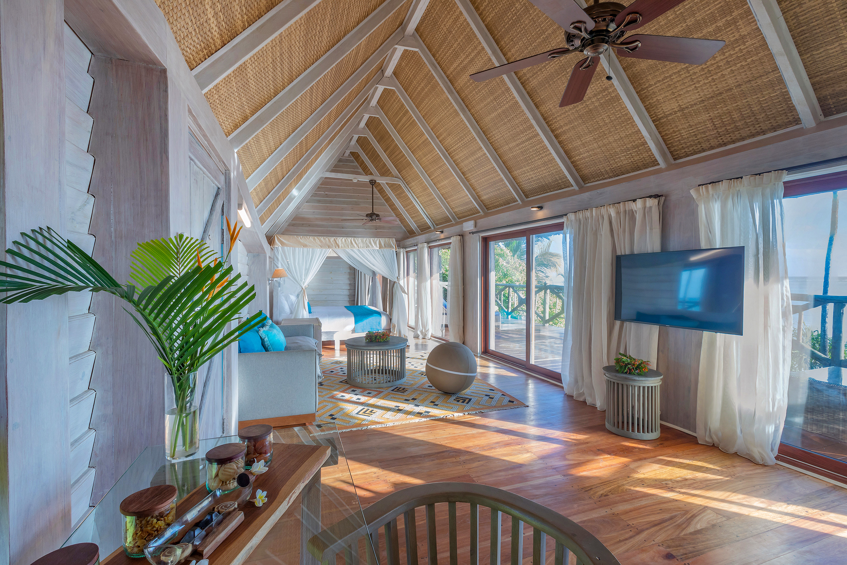 Spacious tropical resort suite with vaulted rattan ceiling, bed, and balcony.