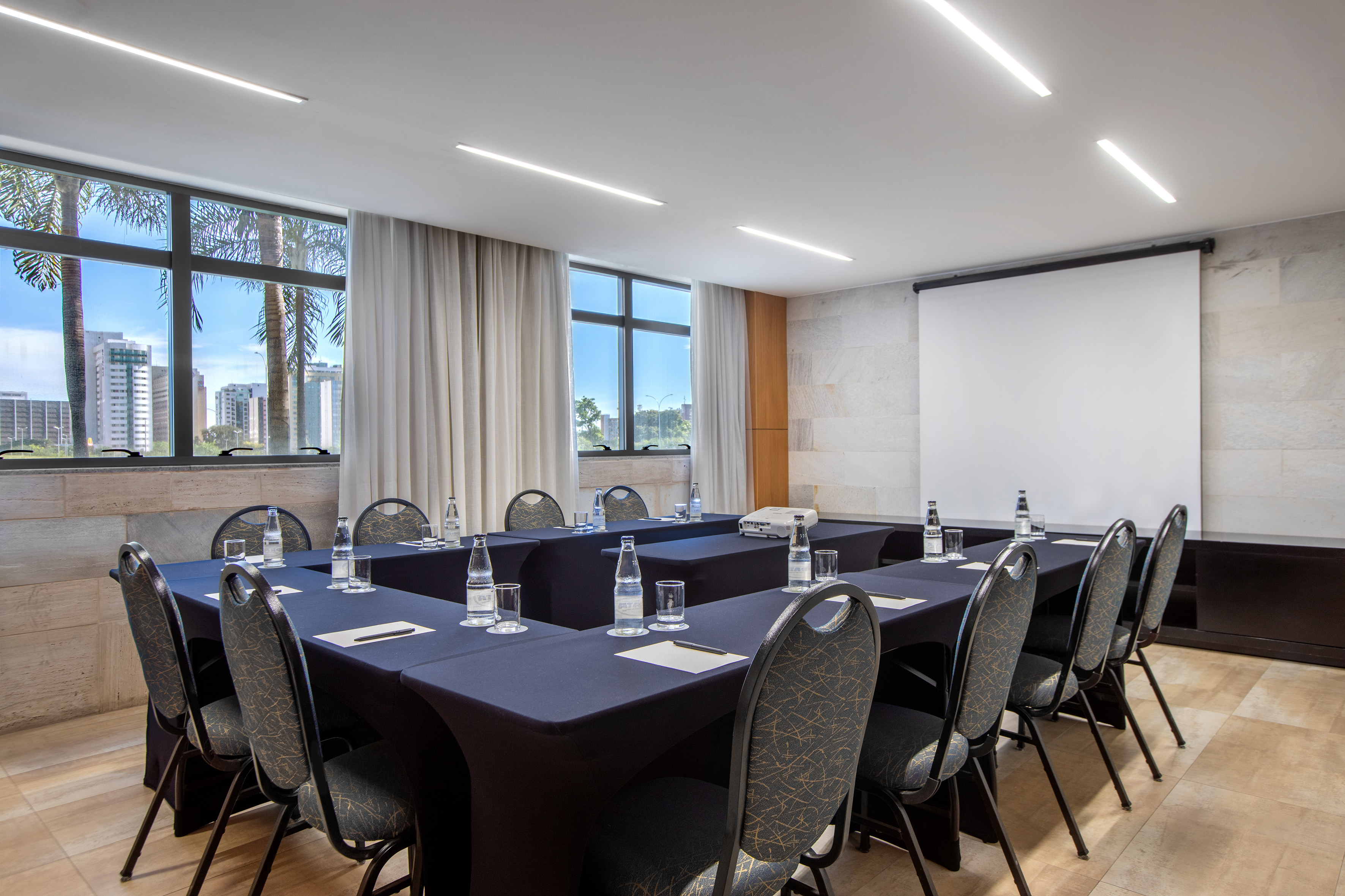Modern conference room with U-shaped table, projector, and city view windows.