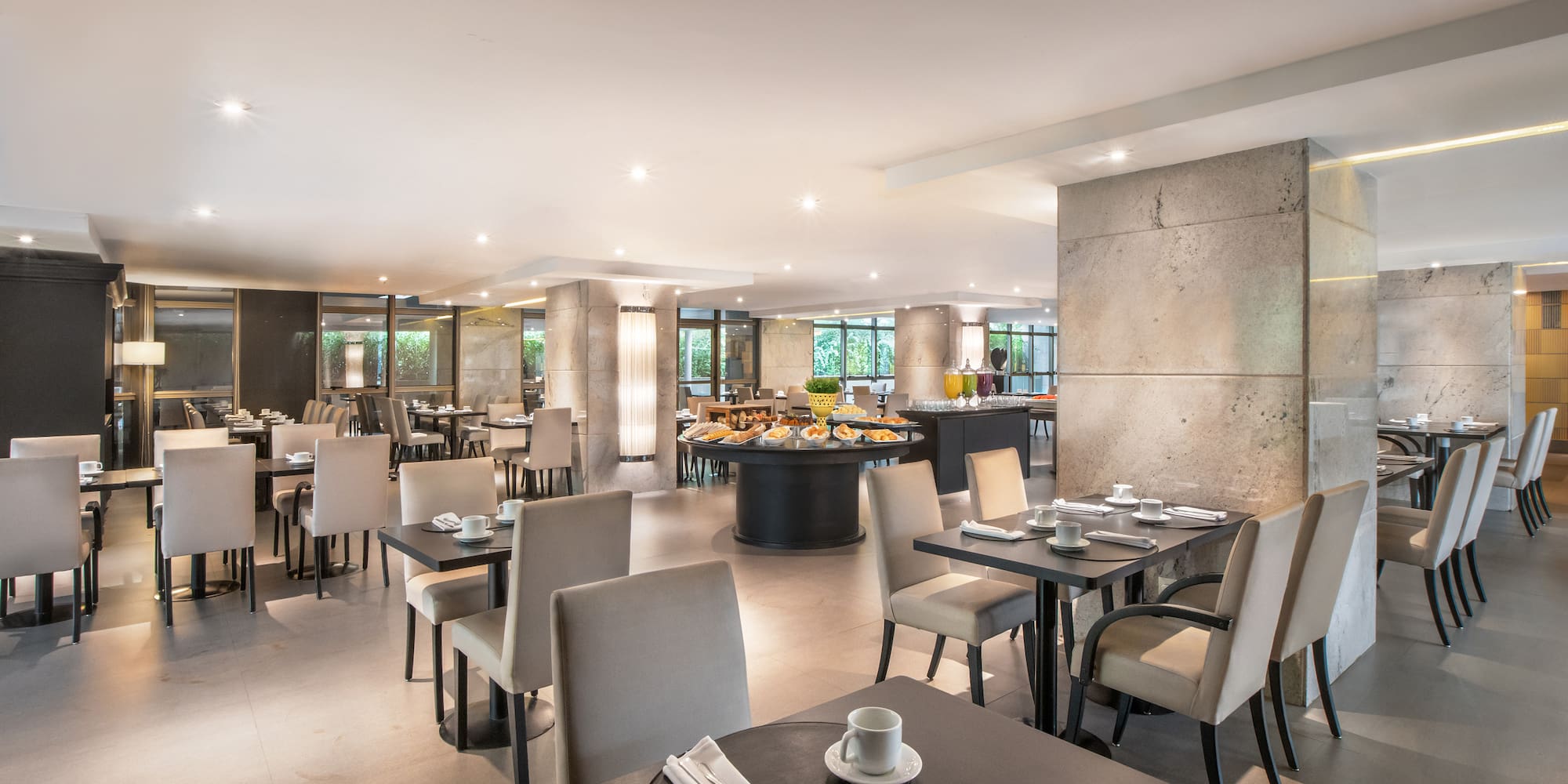 Elegant hotel restaurant with breakfast buffet and set dining tables.