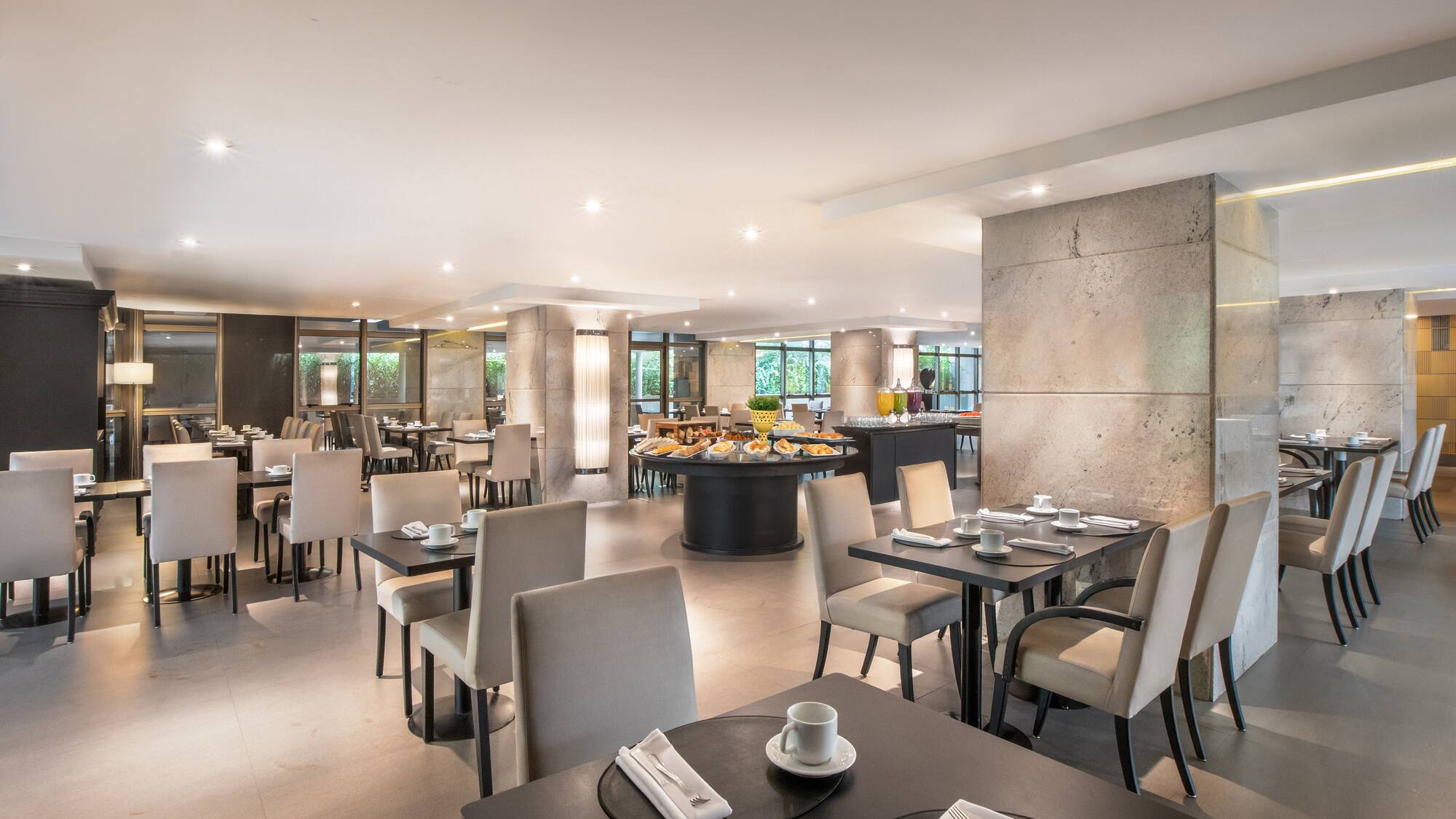 Elegant hotel restaurant with breakfast buffet and set dining tables.