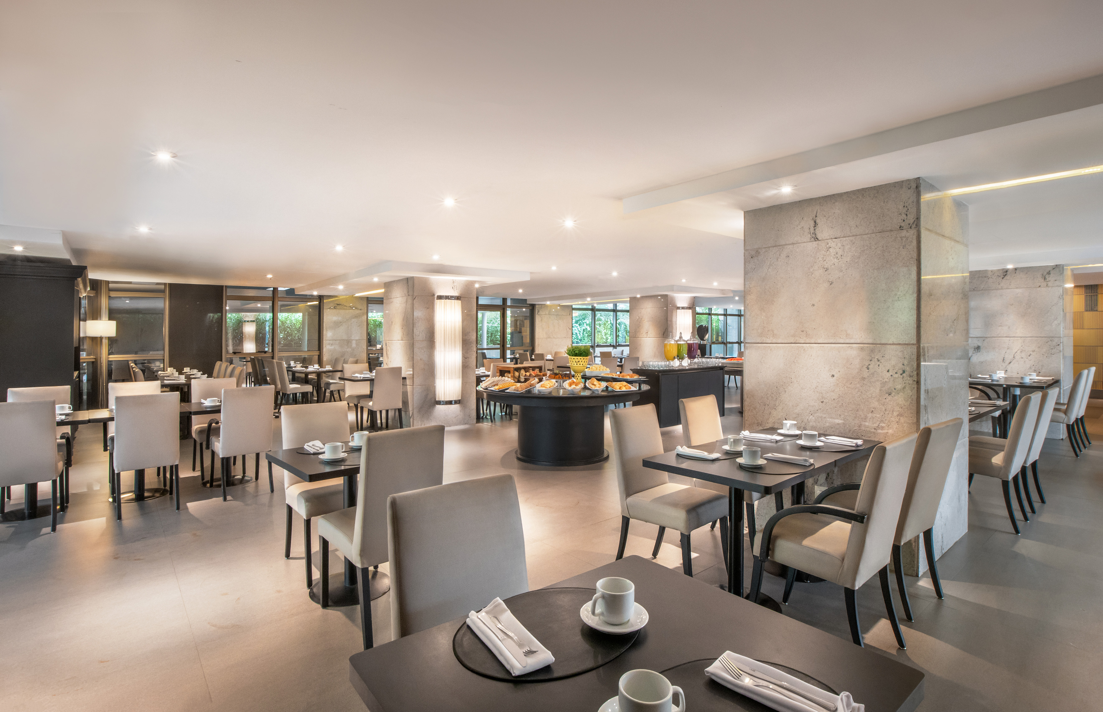 Elegant hotel restaurant with breakfast buffet and set dining tables.