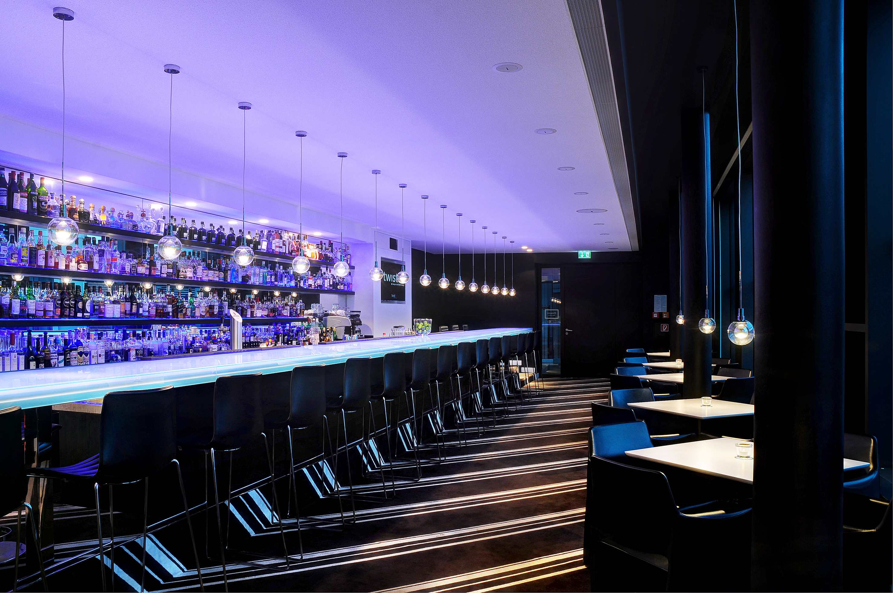 Contemporary bar with purple light, liquor bottles, black bar stools, and tables.