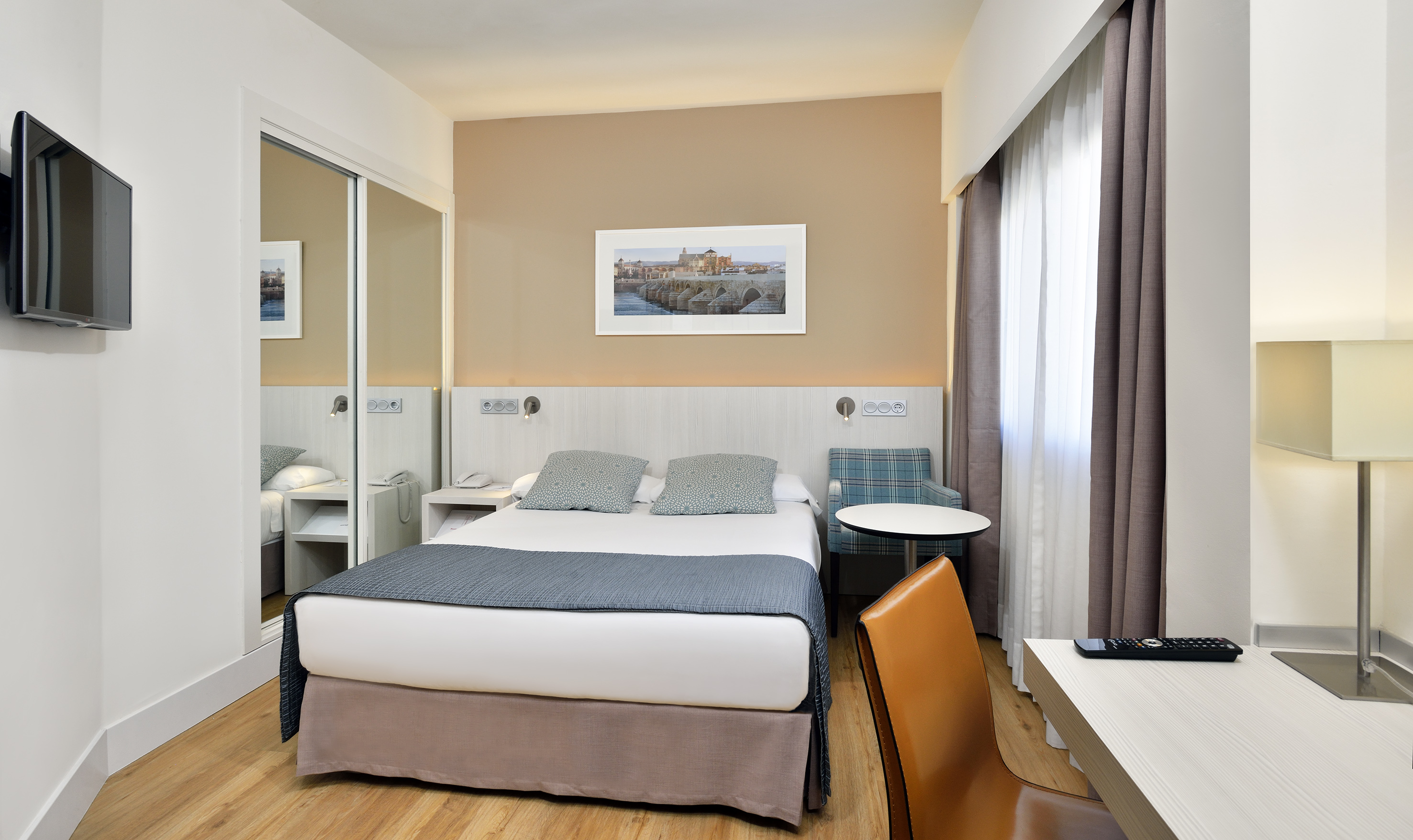 Modern hotel room with queen bed, desk, TV, and mirrored closet.