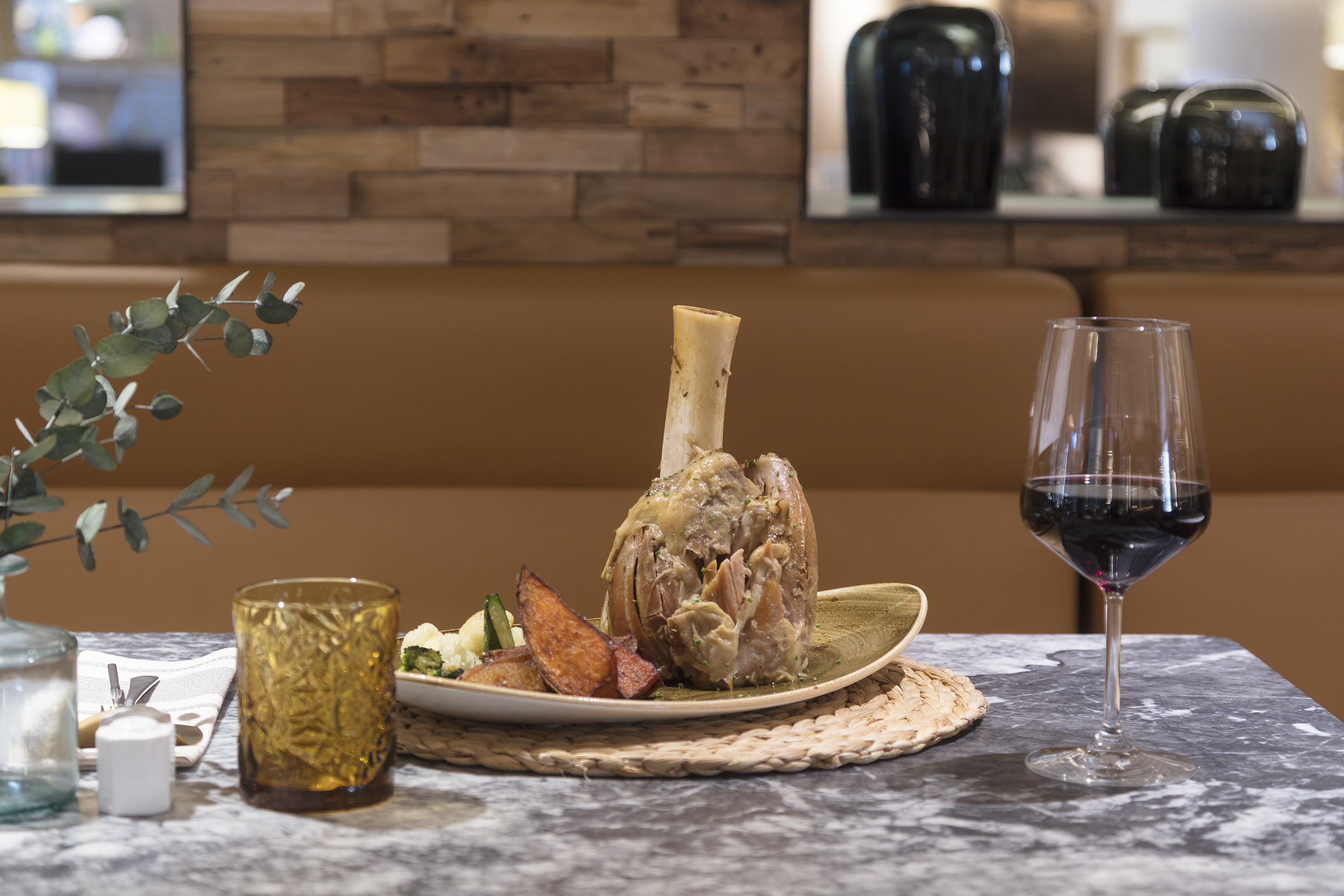 Lamb shank with roasted vegetables and red wine on a restaurant table.