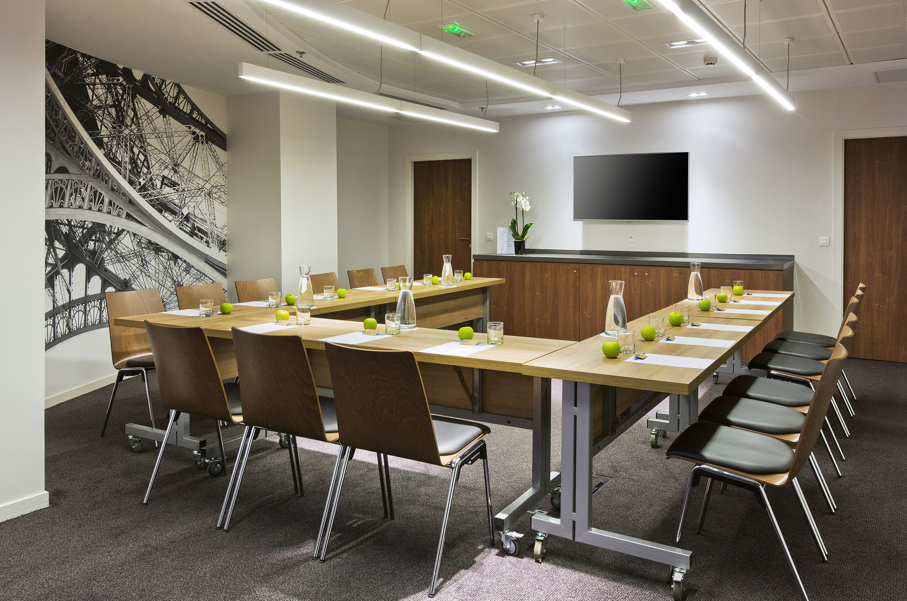 Modern meeting room with U-shaped tables, TV screen, Eiffel Tower mural.