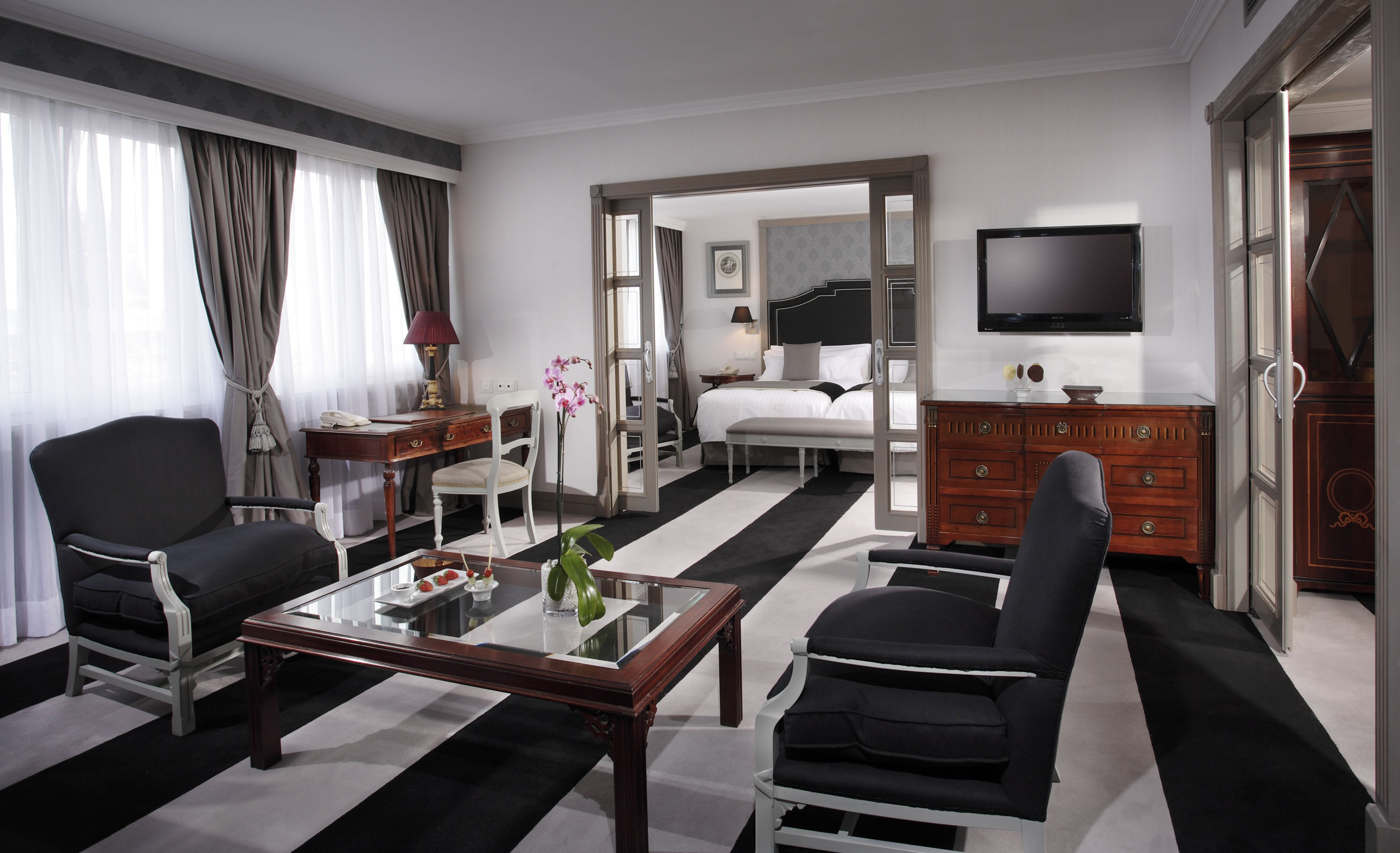 Elegant hotel suite: living area, bedroom, black & white striped rug.