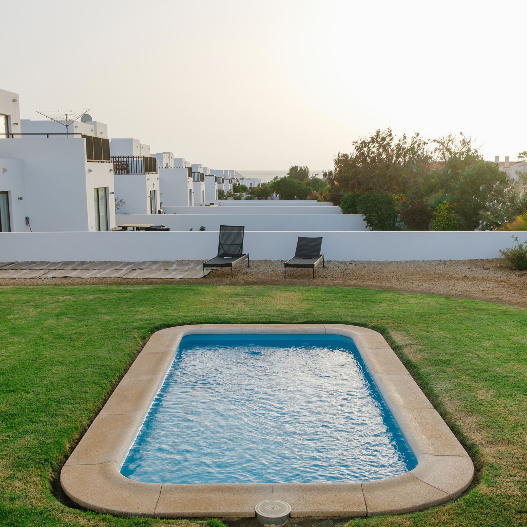 a pool in a yard with white buildings in the background