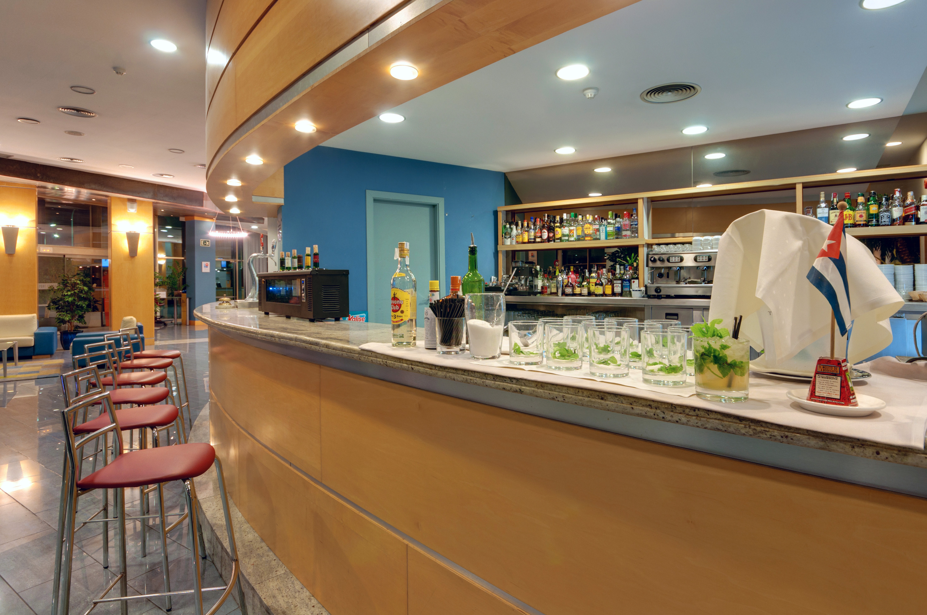 Modern hotel bar with red stools, cocktail glasses, and liquor bottles.