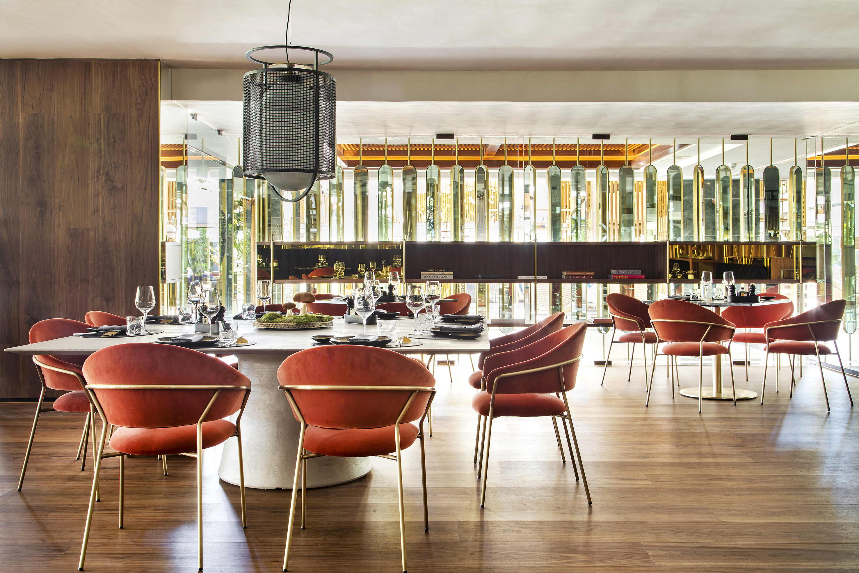 Modern dining room with long table, rust velvet chairs, and elegant decor.