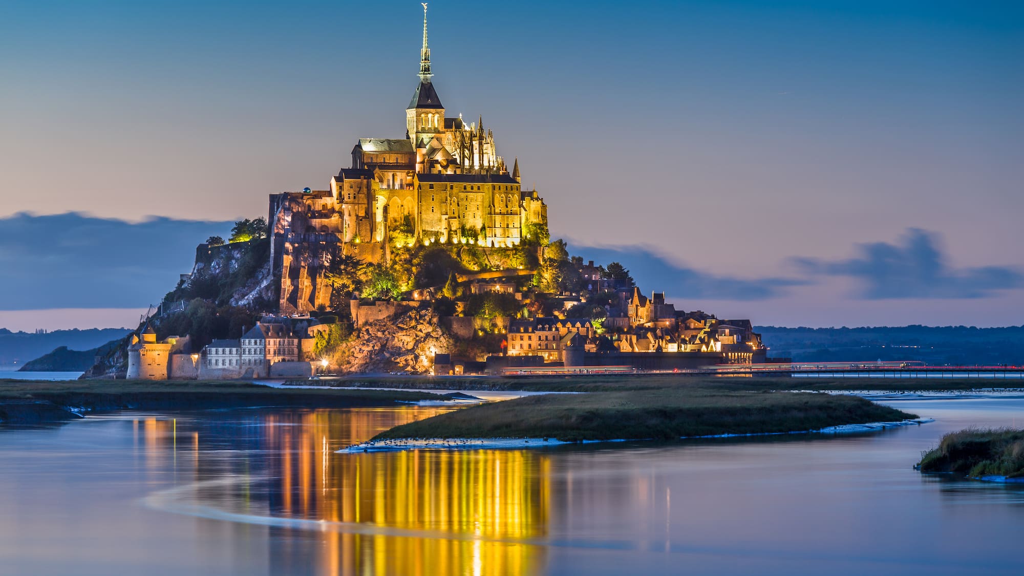 a castle on a hill with lights on it with Mont Saint-Michel in the background