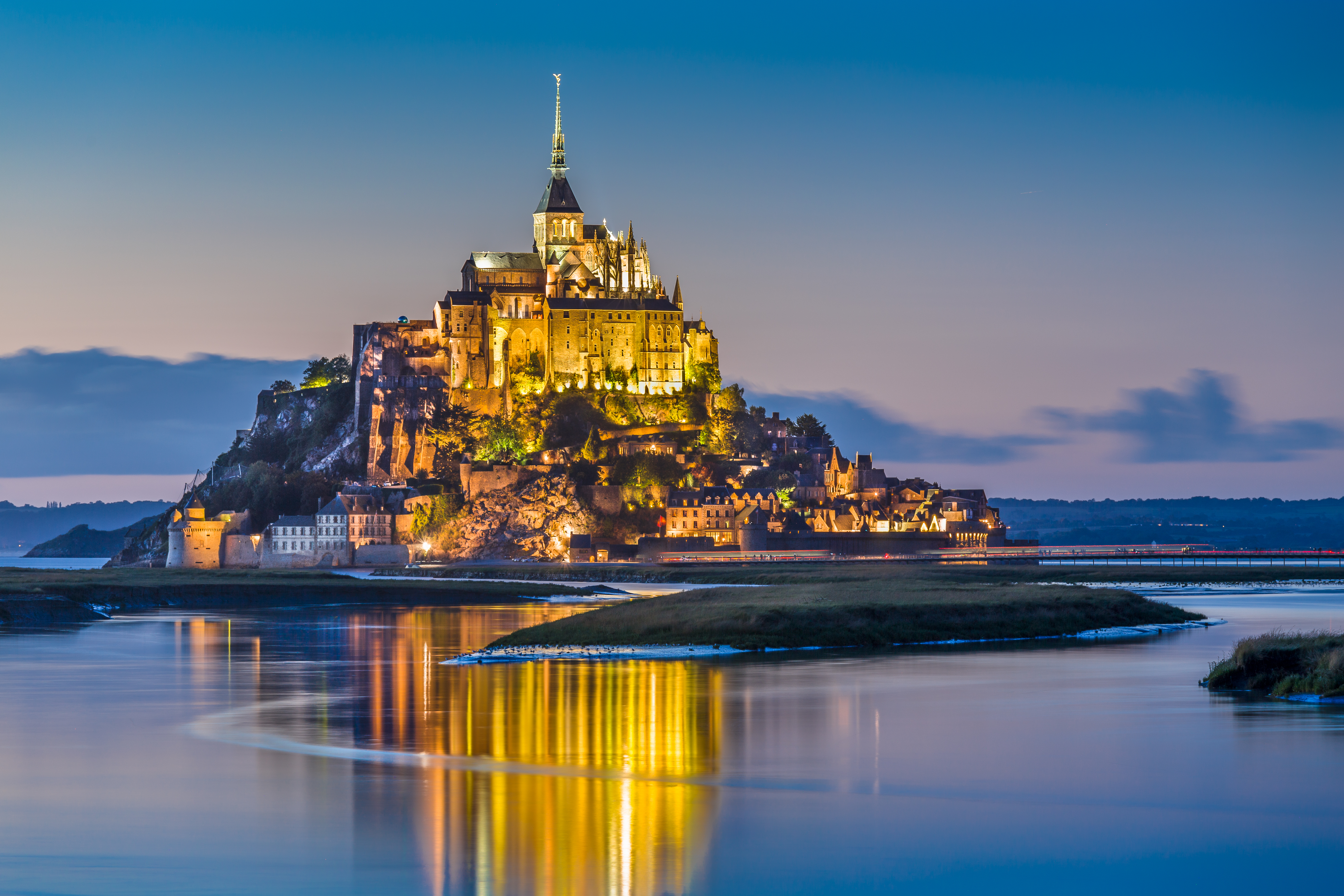 a castle on a hill with lights on it with Mont Saint-Michel in the background