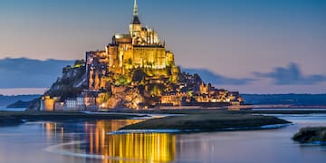 a castle on a hill with lights on it with Mont Saint-Michel in the background