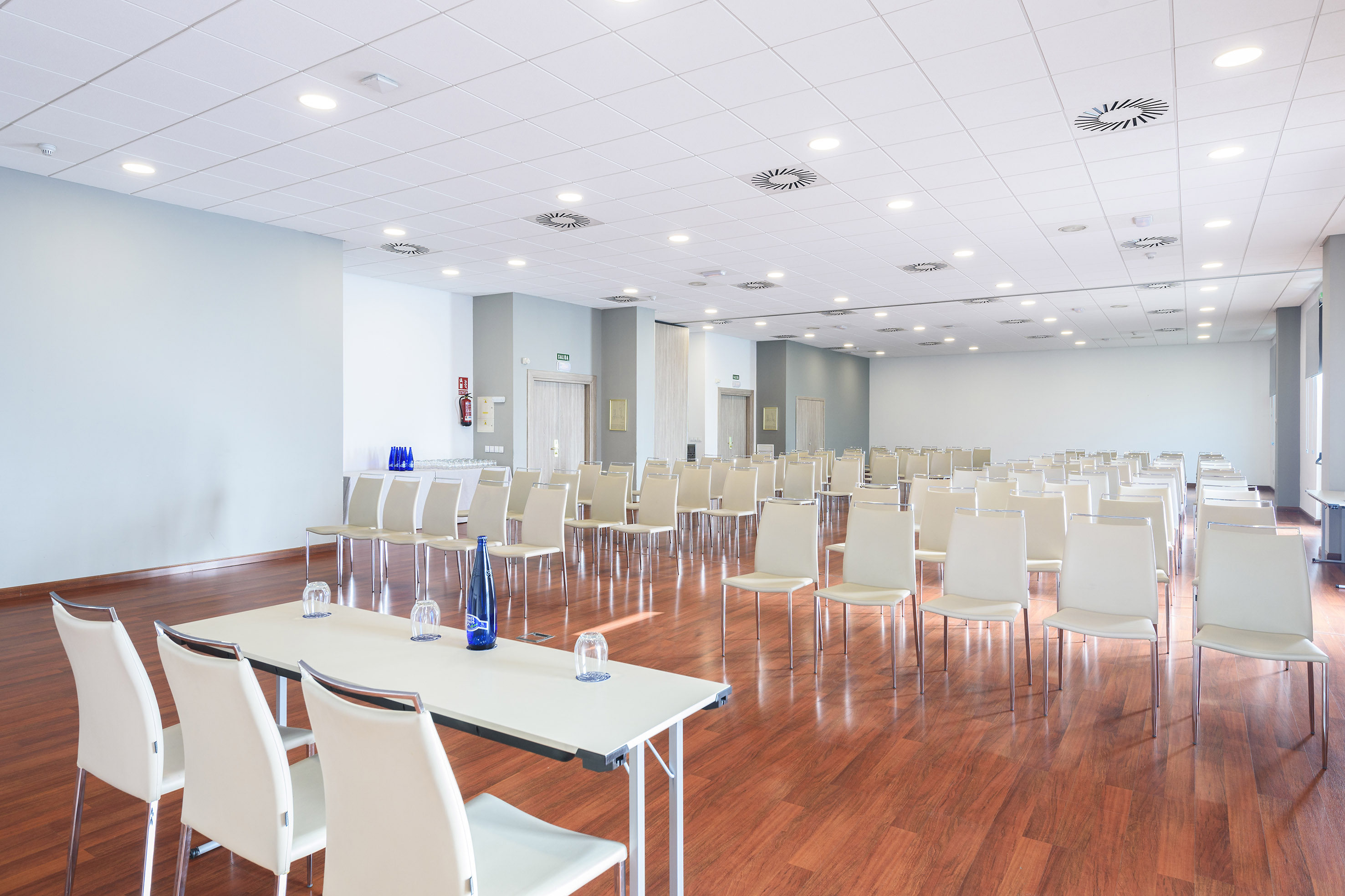 Modern conference room with organized rows of white chairs and wooden floor.