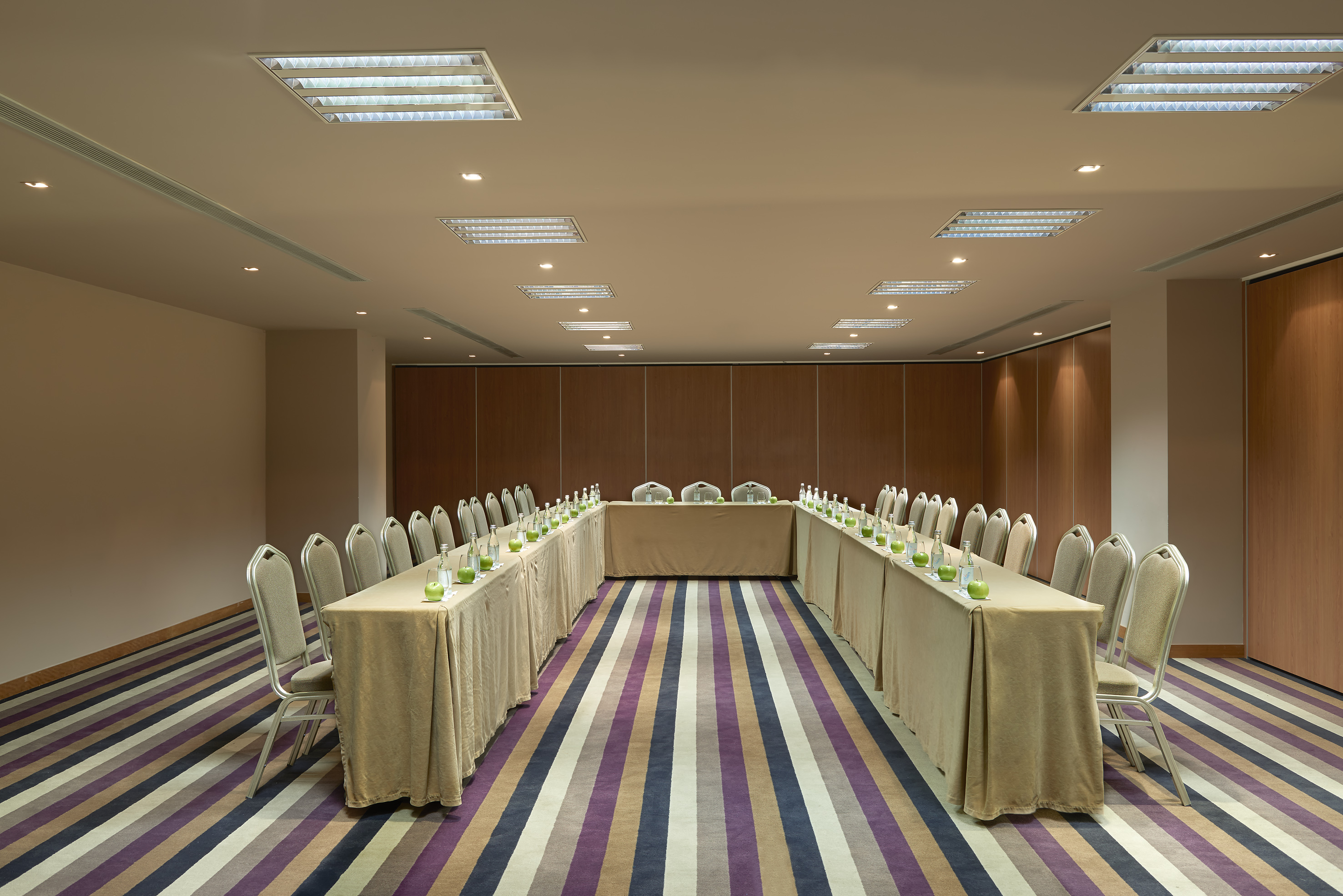 U-shaped meeting room with tables, chairs, water bottles, and striped carpet.
