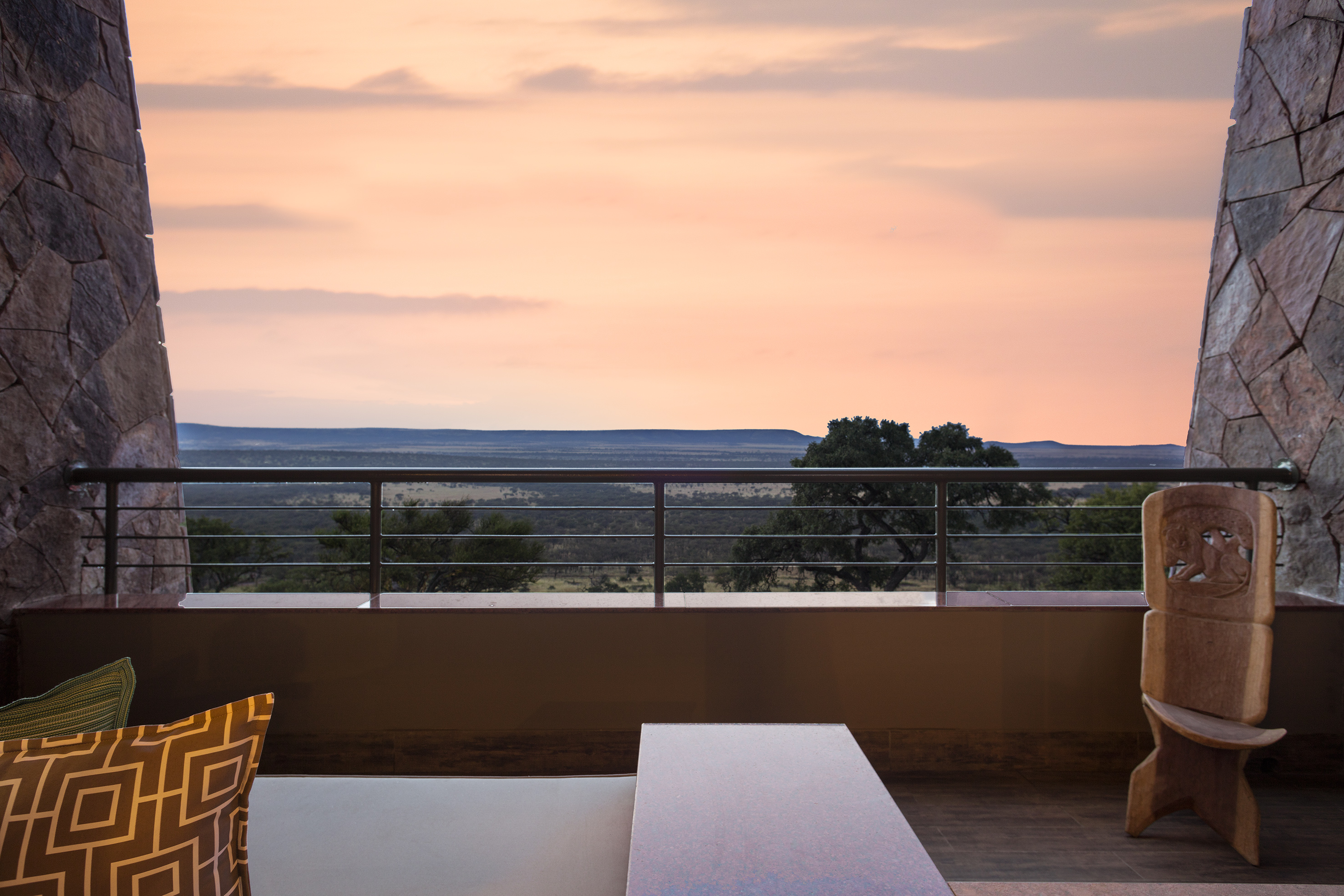 Stone balcony overlooking vast African savanna during a colorful sunset.