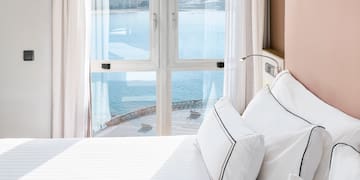 a bed with white sheets and pillows in a room with a view of water and a city