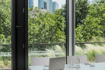 a table with chairs and laptops in a room with trees and a city view
