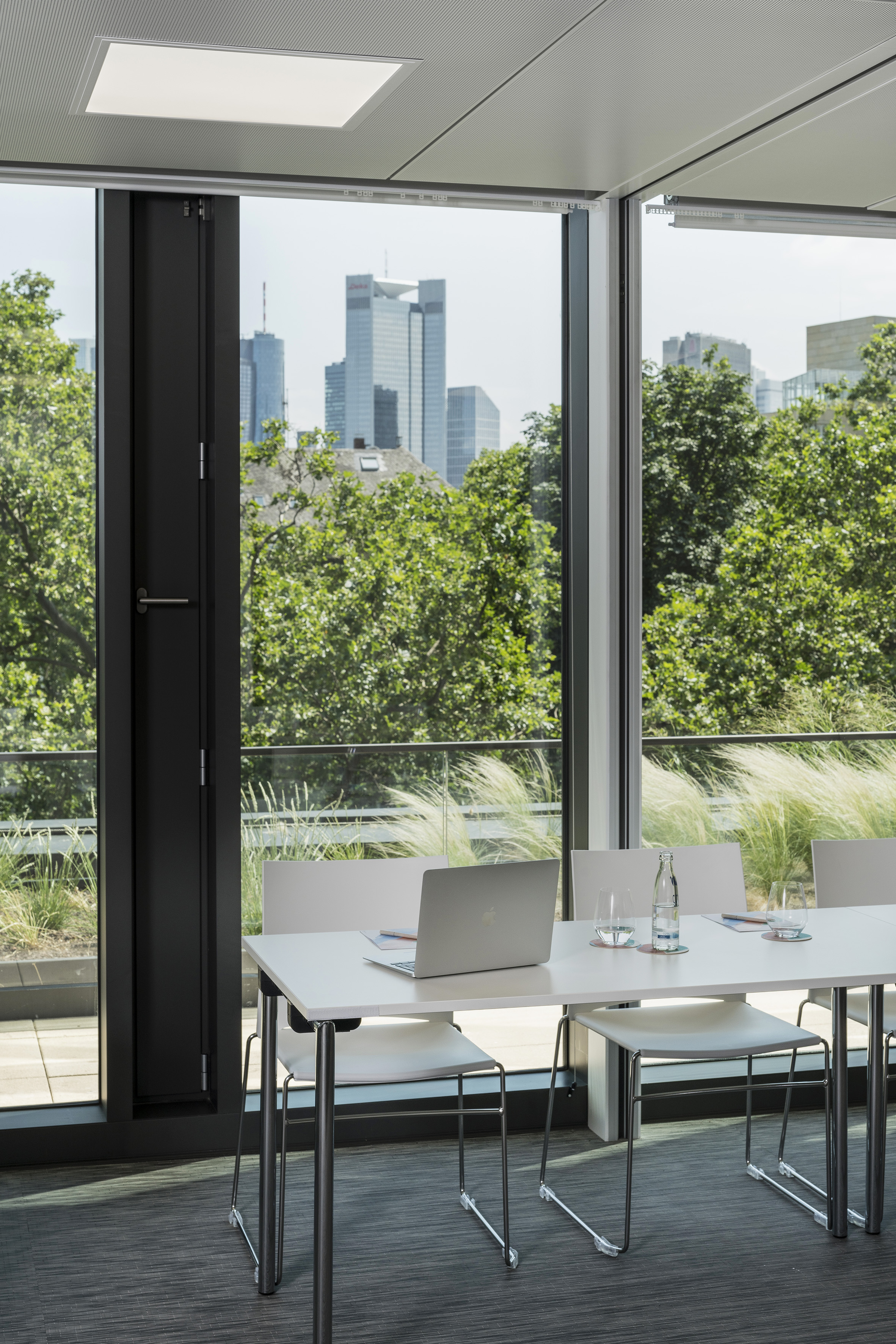 a table with chairs and laptops in a room with trees and a city view