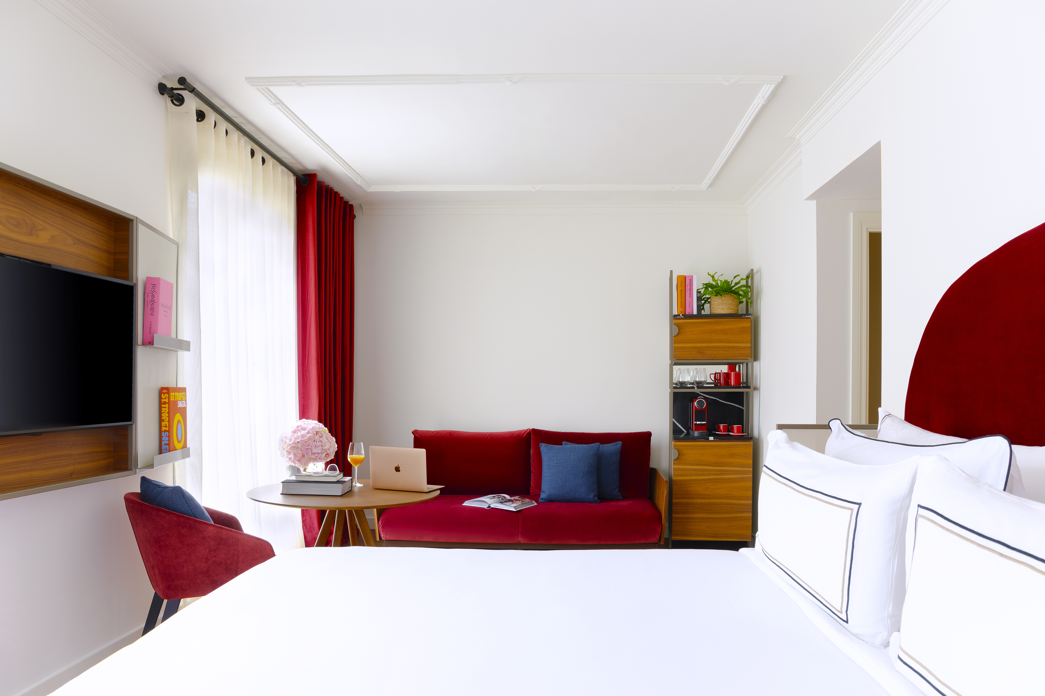 Luxury hotel suite featuring a king bed, red sofa, work area, and coffee station.