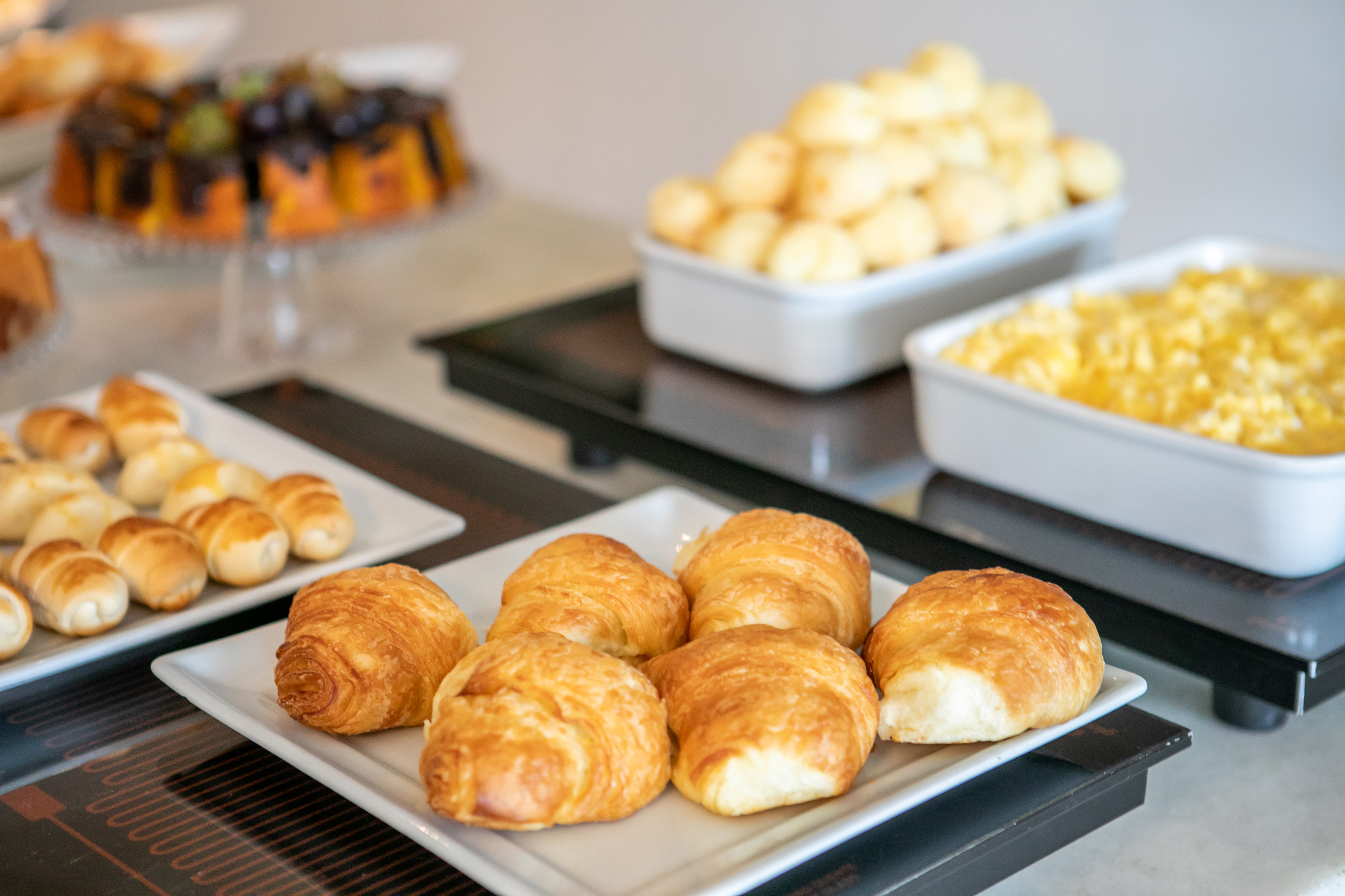 Golden croissants, pão de queijo, scrambled eggs at breakfast buffet.
