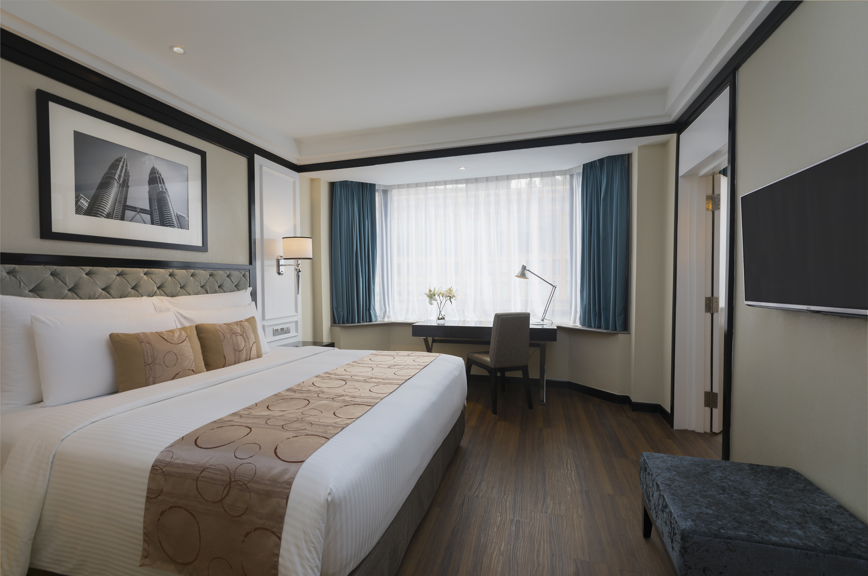 Modern hotel room with king bed, desk by bay window, Petronas Towers art.