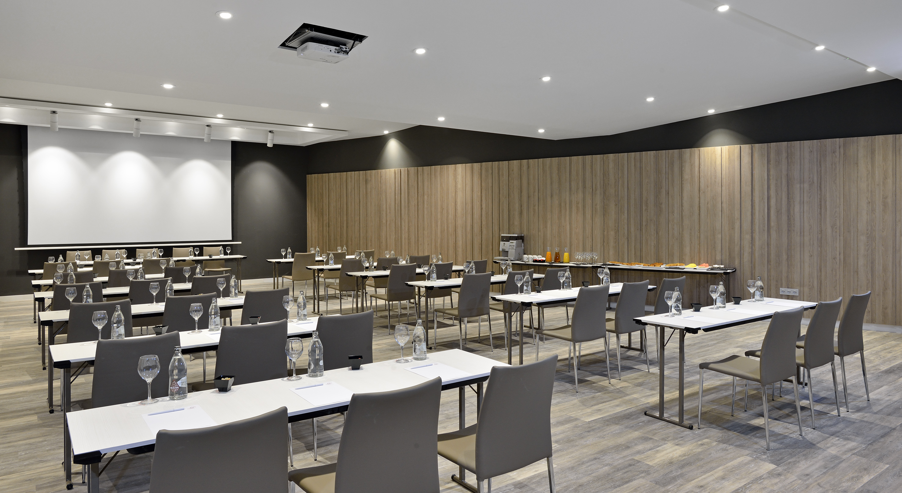 Modern conference room with screen, tables, chairs, and refreshments.