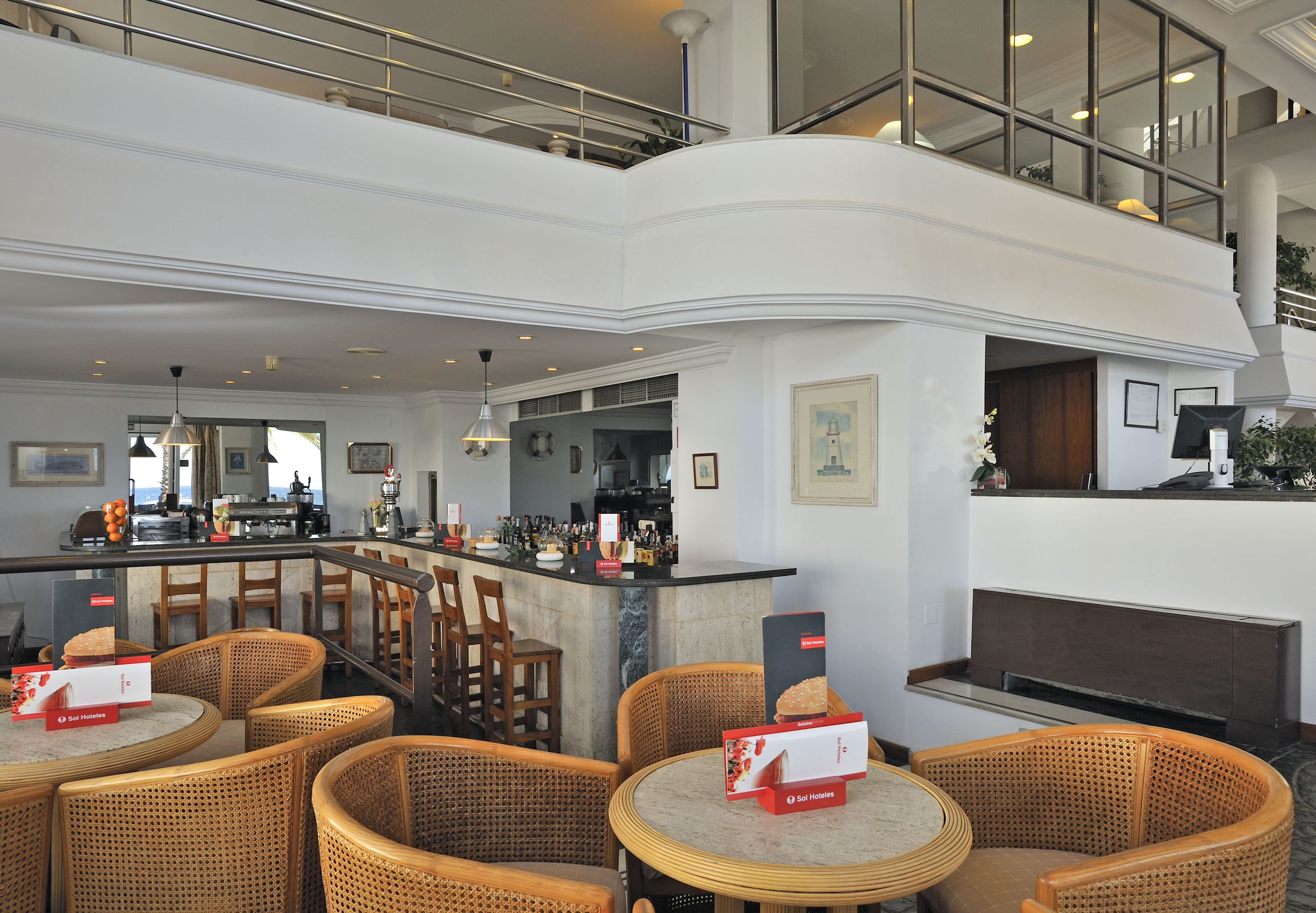 Bright hotel lounge bar with wicker furniture, reception, and sea view.