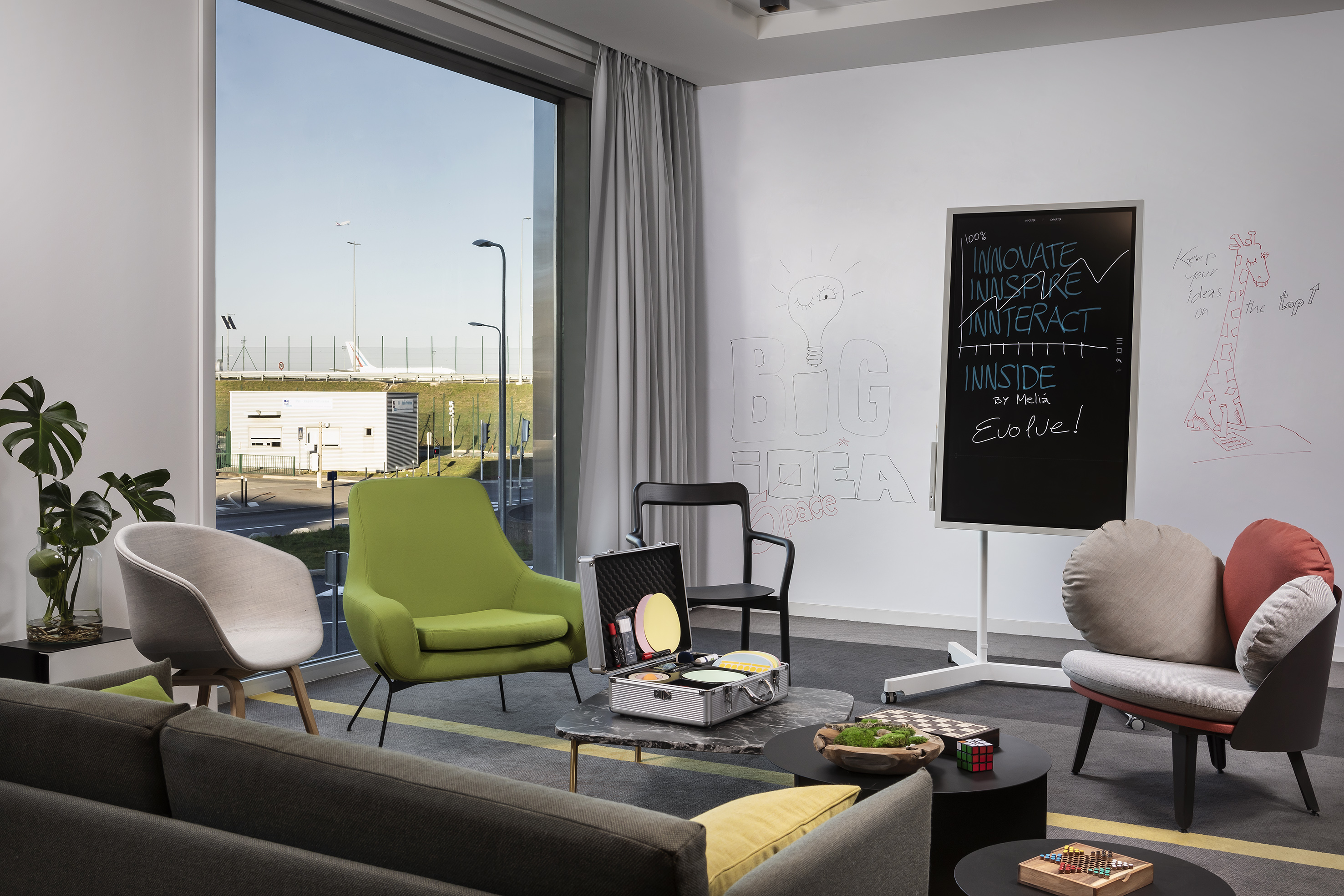 Modern airport lounge with comfortable seating, whiteboard, and runway view.