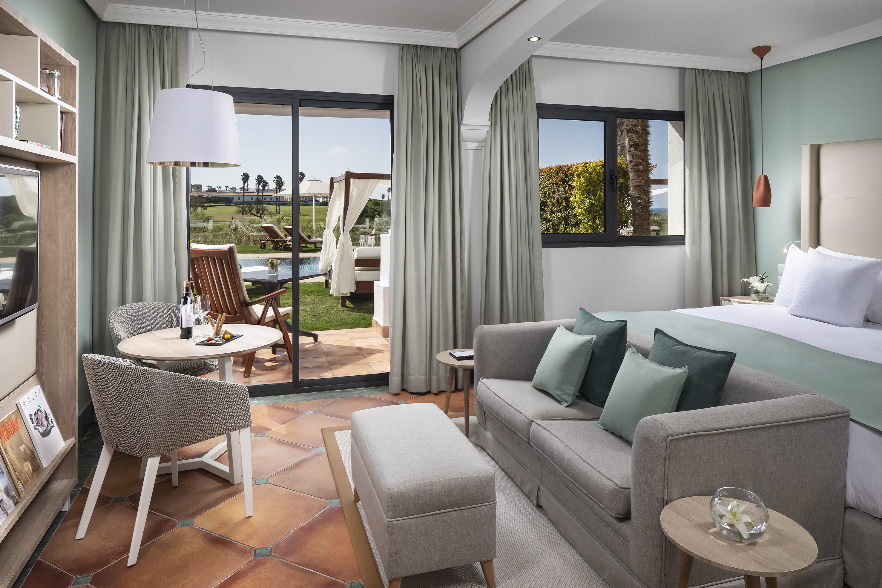 Modern hotel suite with private patio, pool view, and resort landscape.