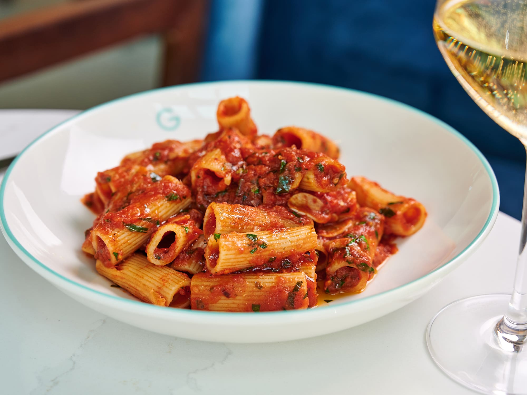 Rigatoni pasta with tomato sauce and herbs, beside a sparkling wine glass.