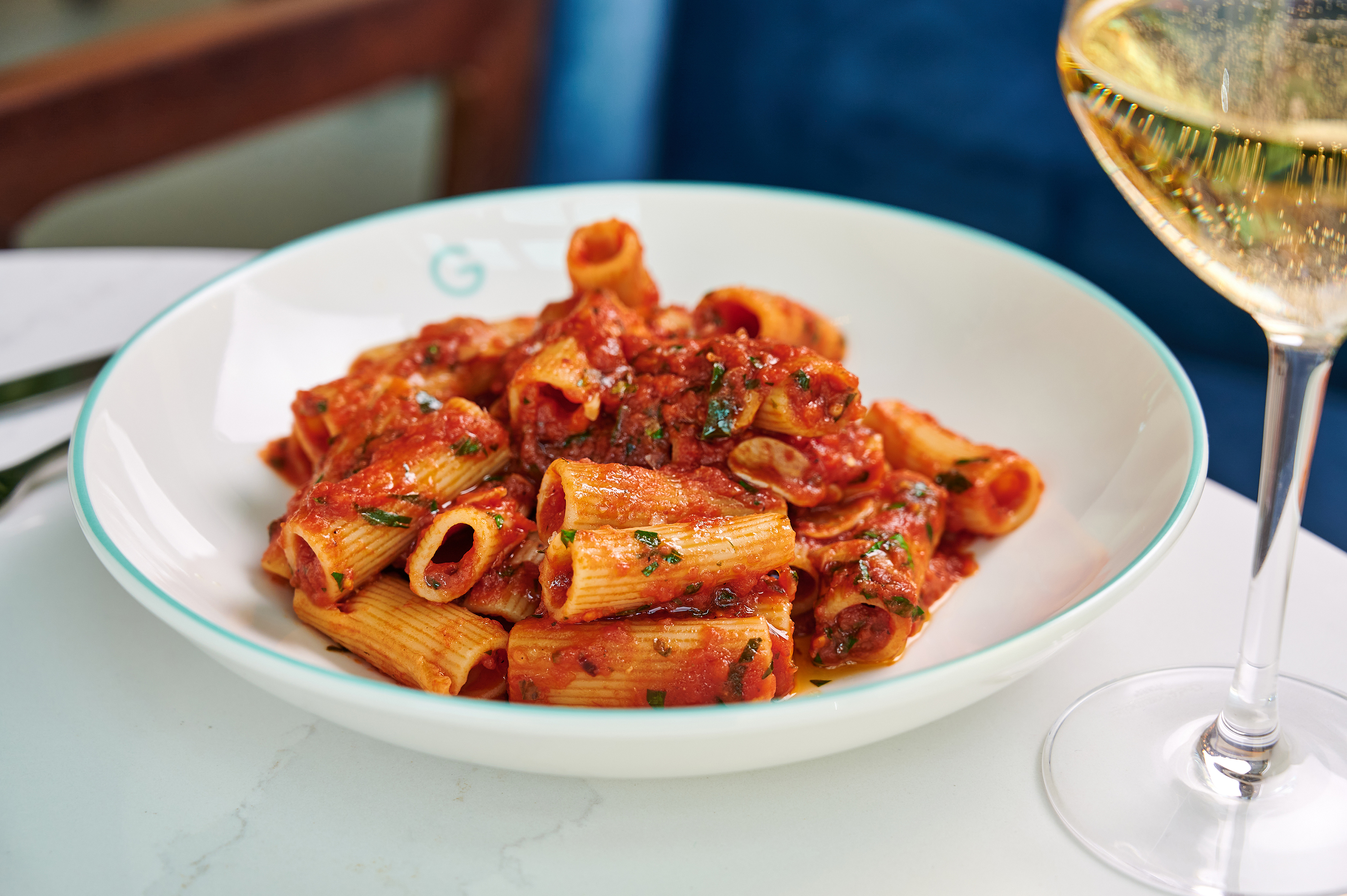 Rigatoni pasta with tomato sauce and herbs, beside a sparkling wine glass.