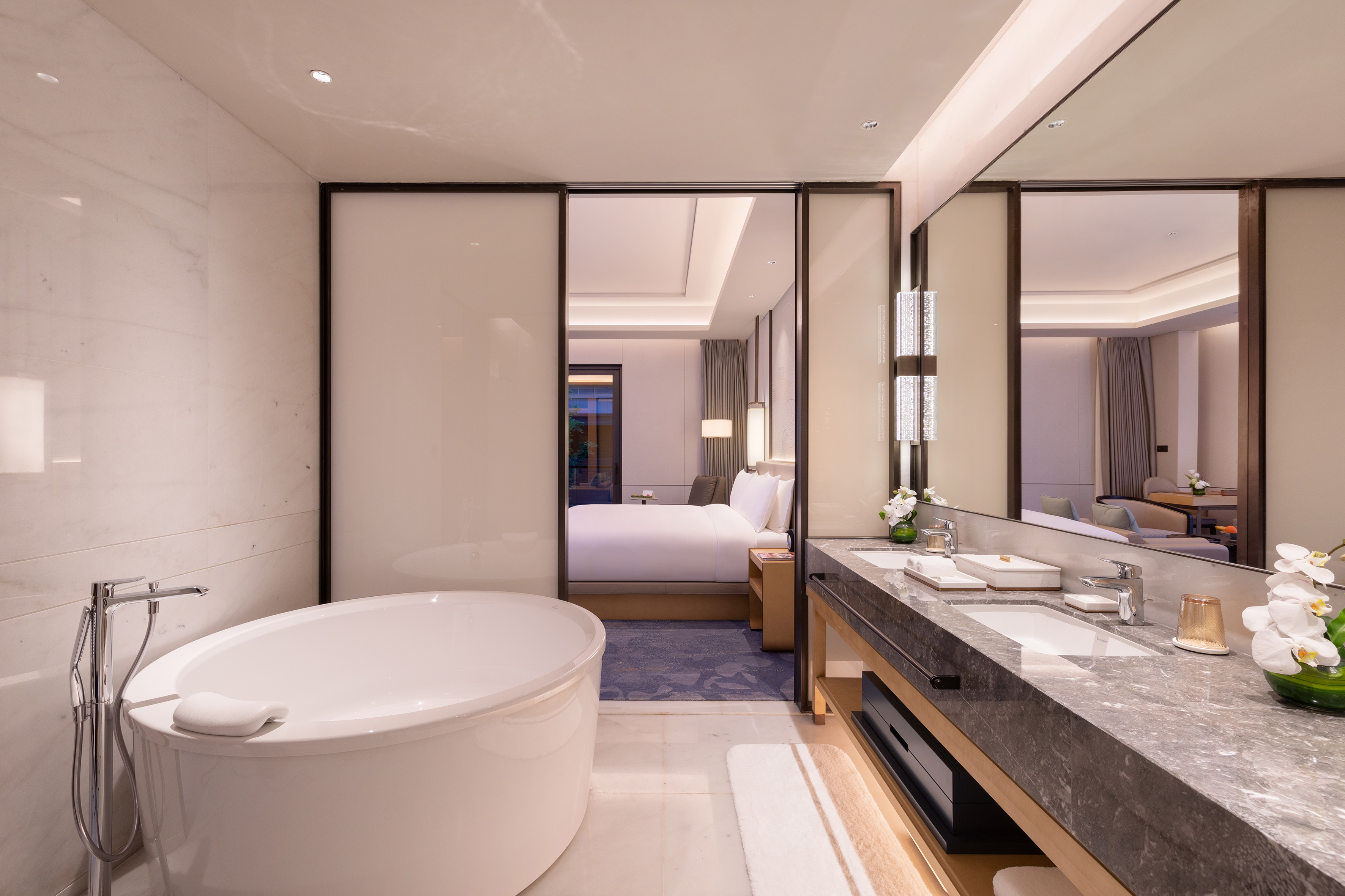 Luxurious hotel bathroom with freestanding tub, double vanity, and bedroom view.