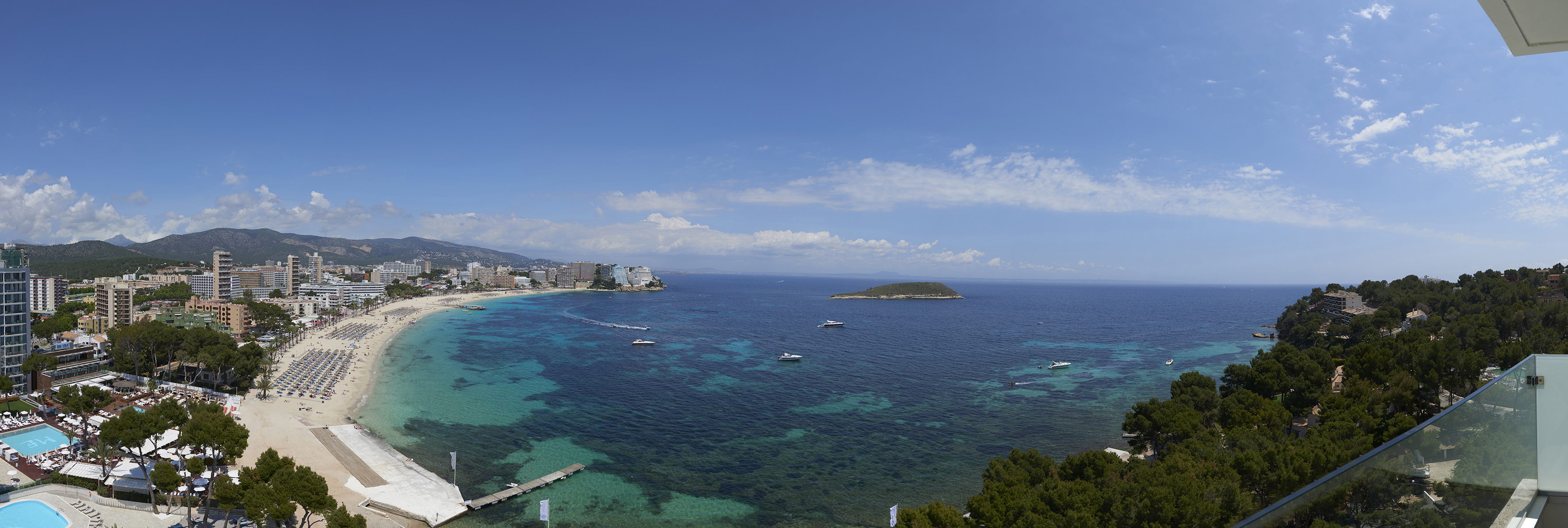 Mallorca panoramic beach, turquoise sea, resort hotels, boats, and island.