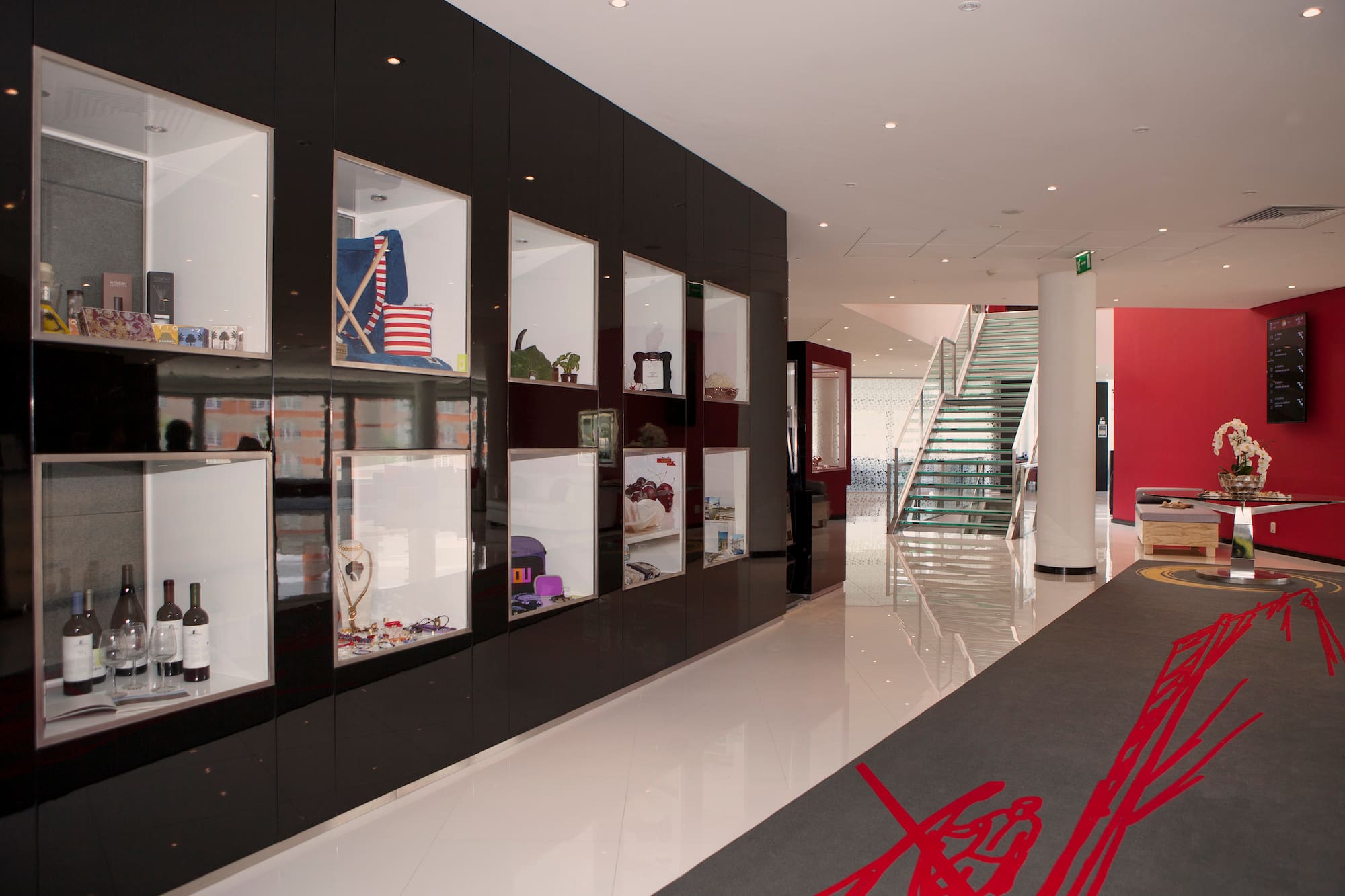 Modern showroom with black display cases, merchandise, glass stairs, and red wall.