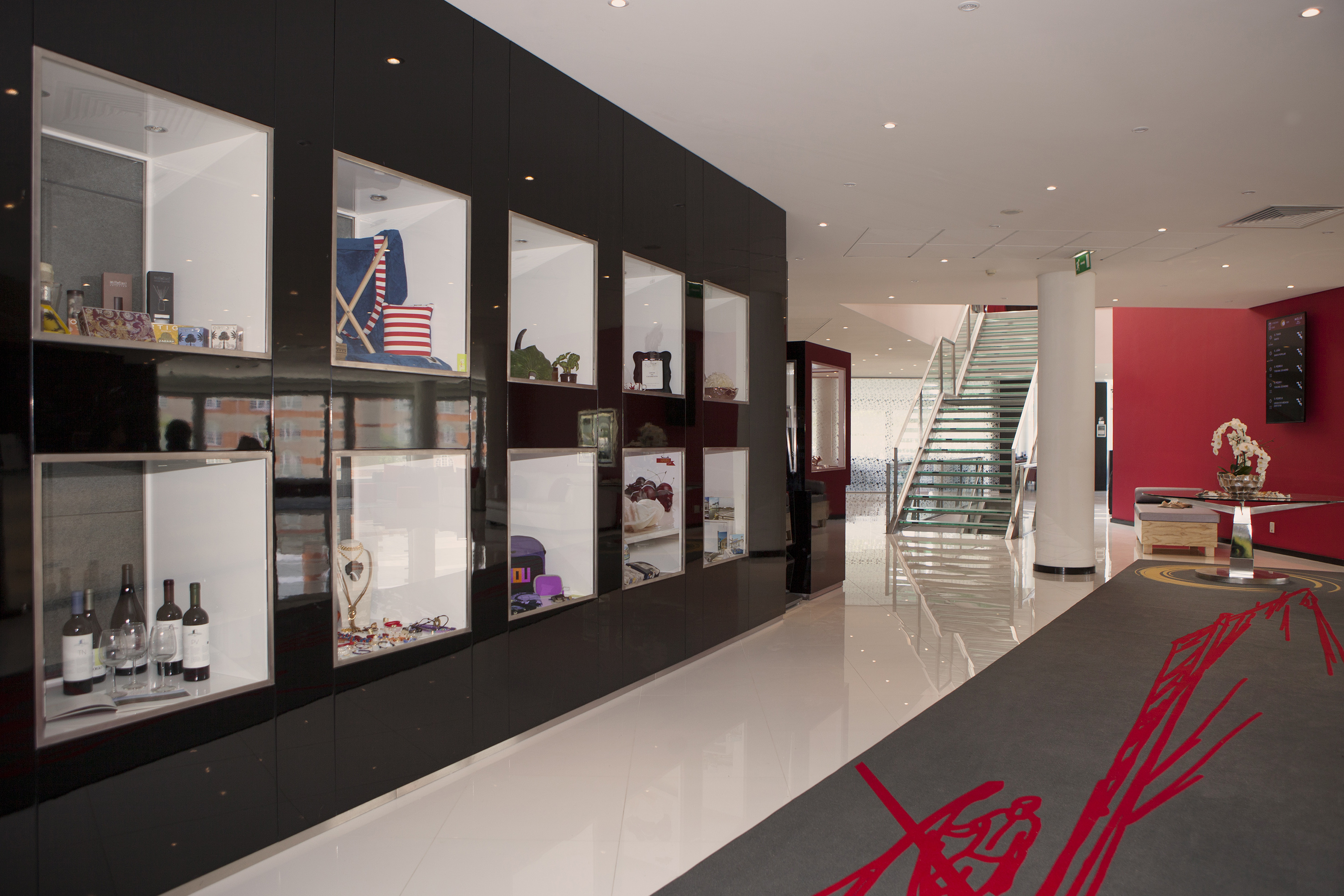 Modern showroom with black display cases, merchandise, glass stairs, and red wall.
