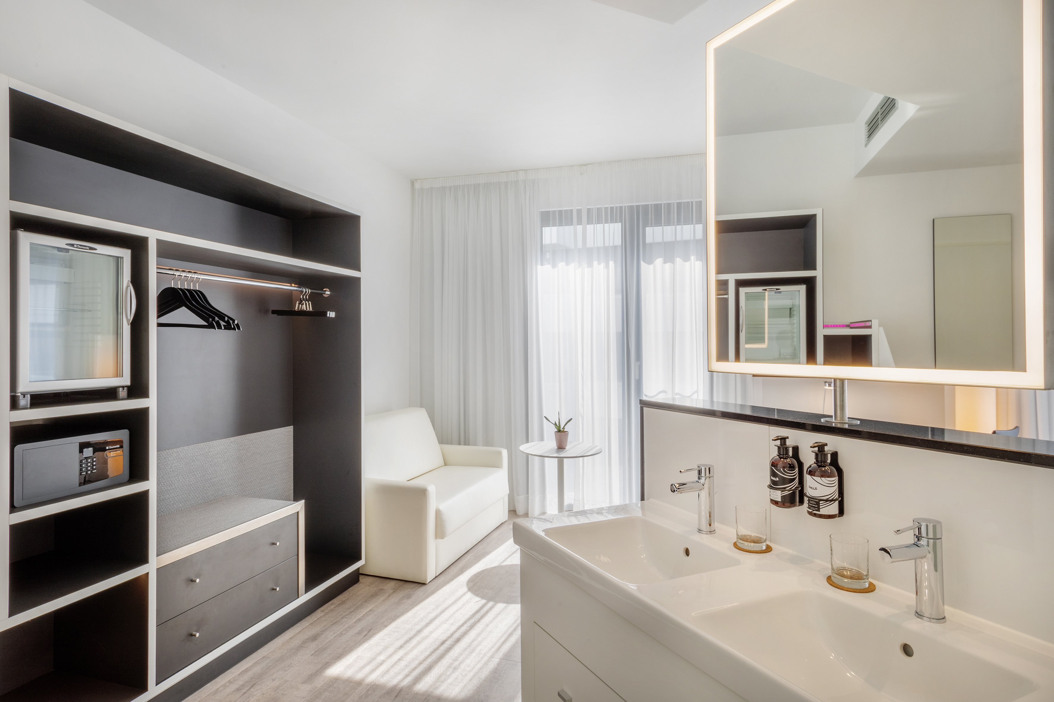 Modern hotel room: double vanity, illuminated mirror, open closet, mini-bar.