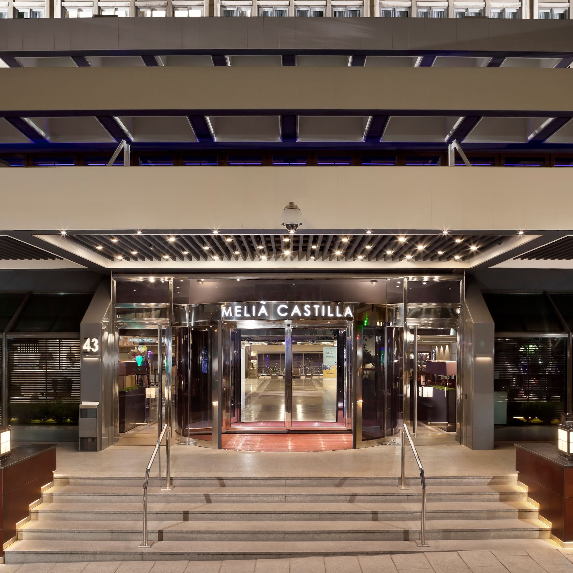 Illuminated Meliá Castilla hotel entrance with modern facade and revolving doors.