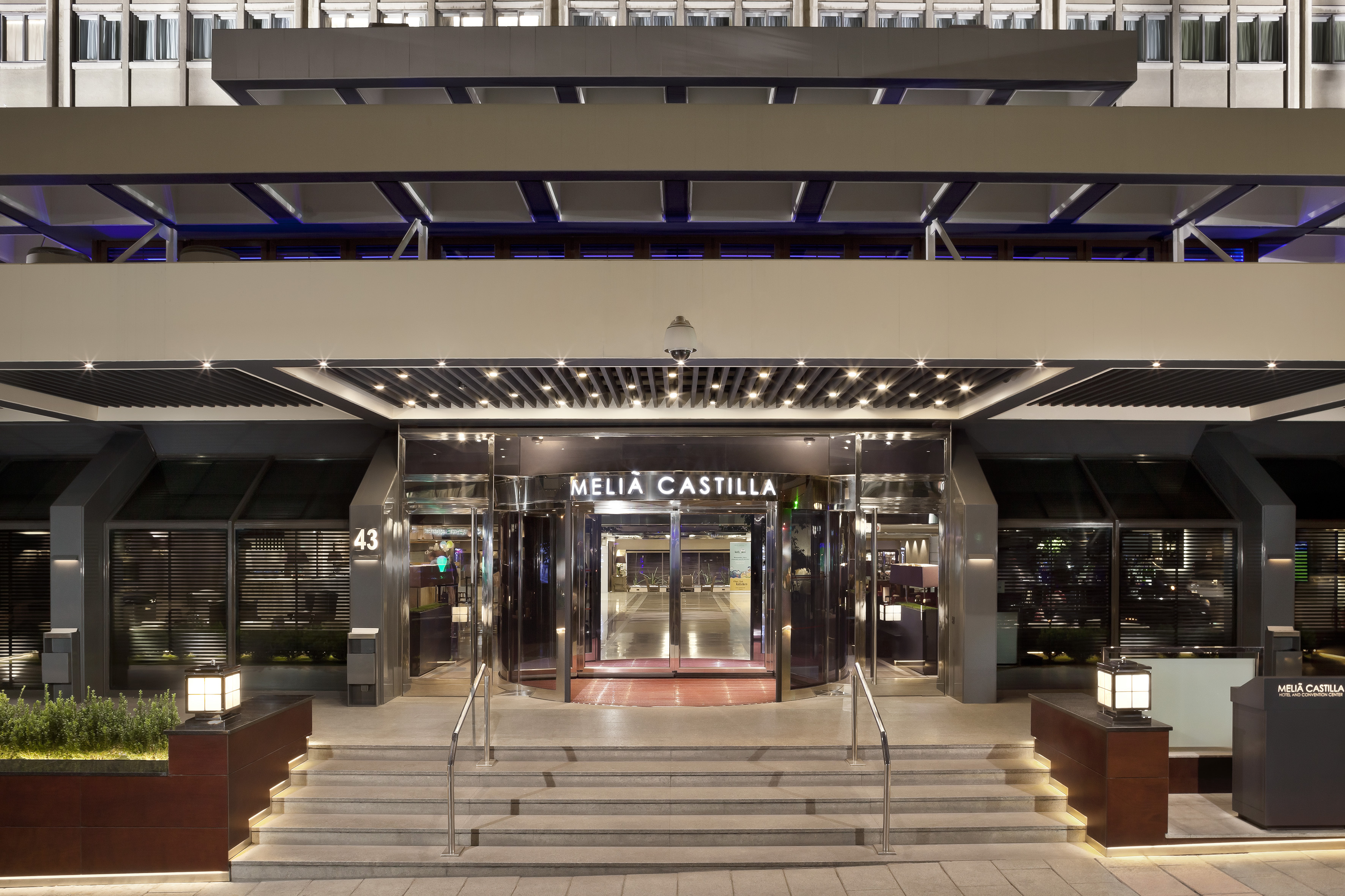 Illuminated Meliá Castilla hotel entrance with modern facade and revolving doors.