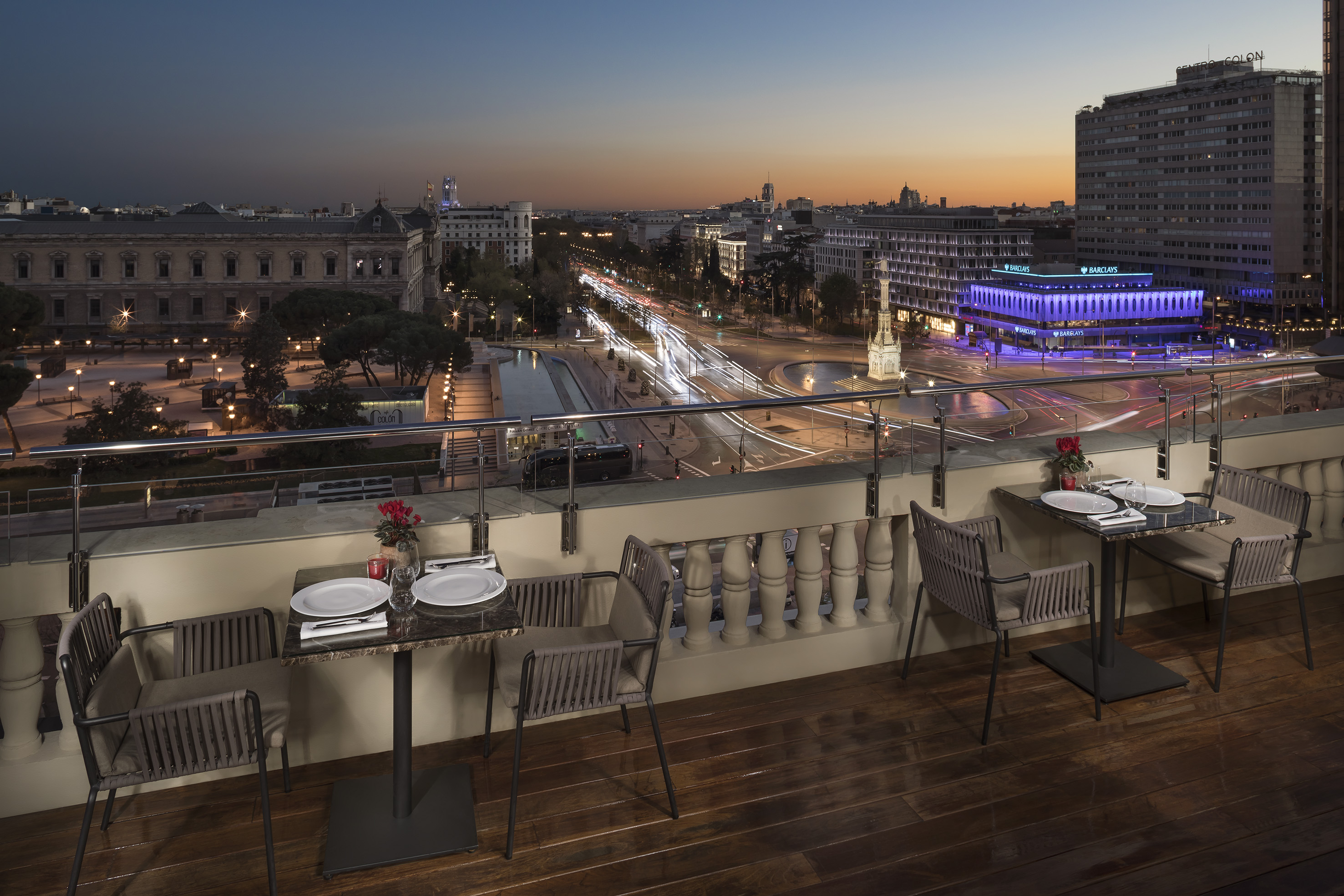 Rooftop restaurant terrace with twilight Madrid city skyline and car light trails.