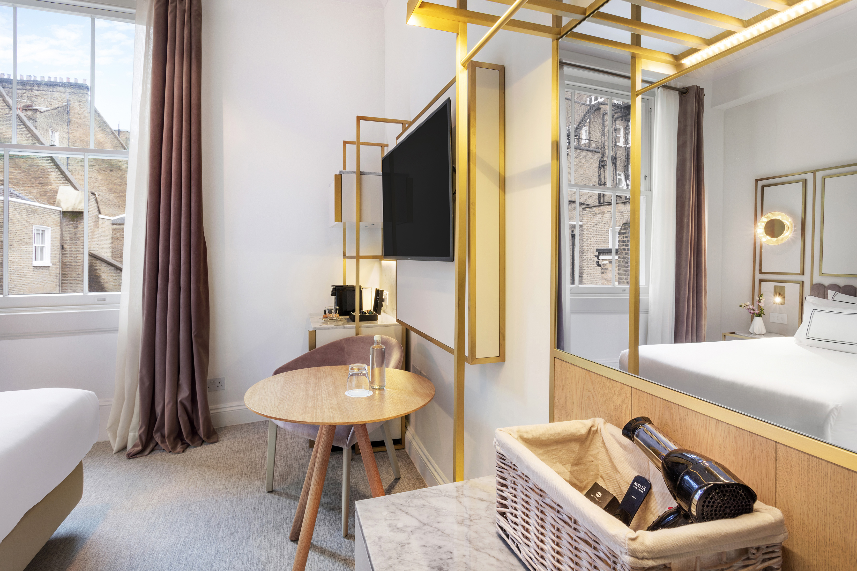 Elegant hotel room with gold details, flat-screen TV, and city window.