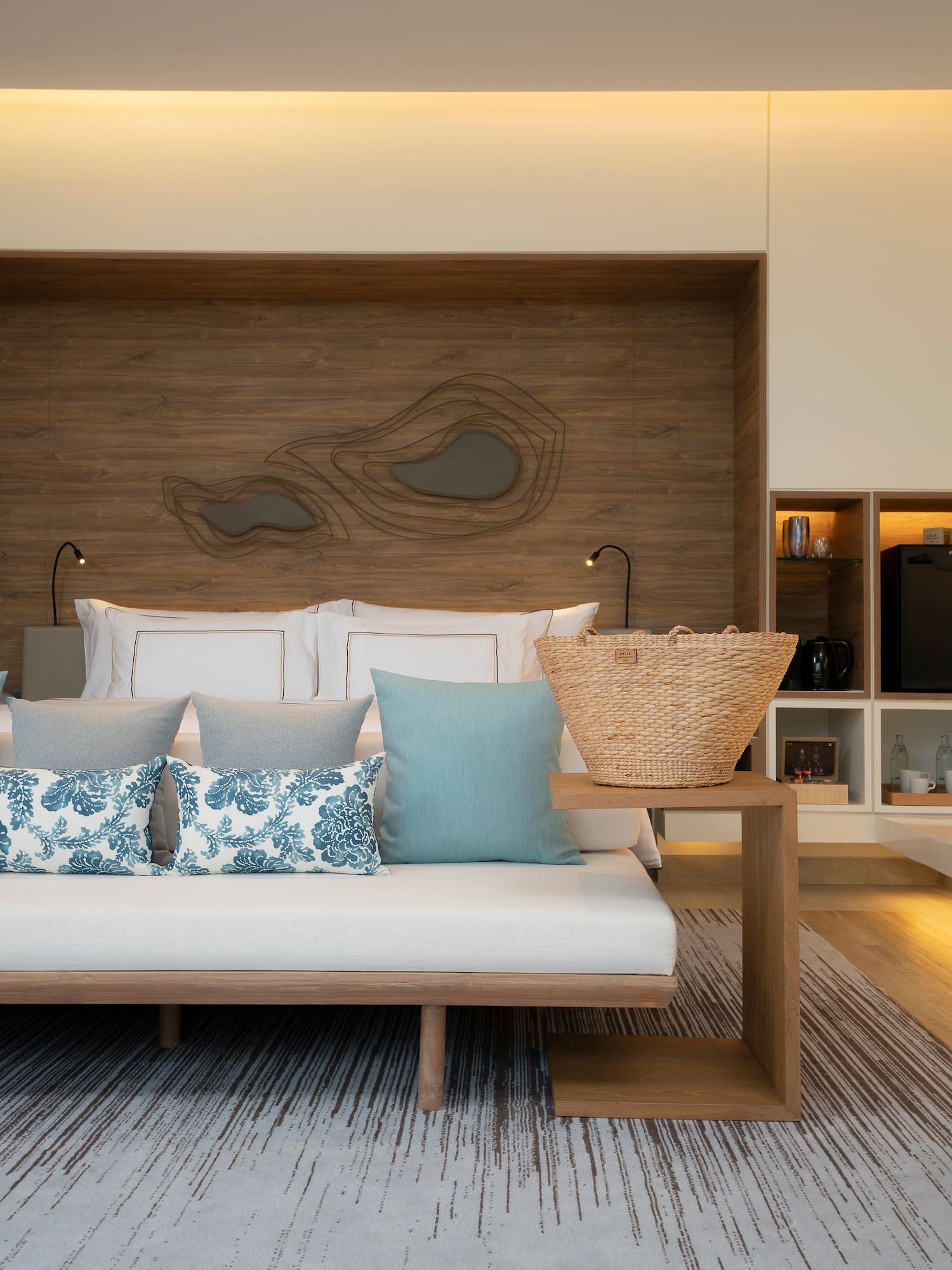 Modern resort room with bed, daybed, blue pillows, wood decor, woven bag.