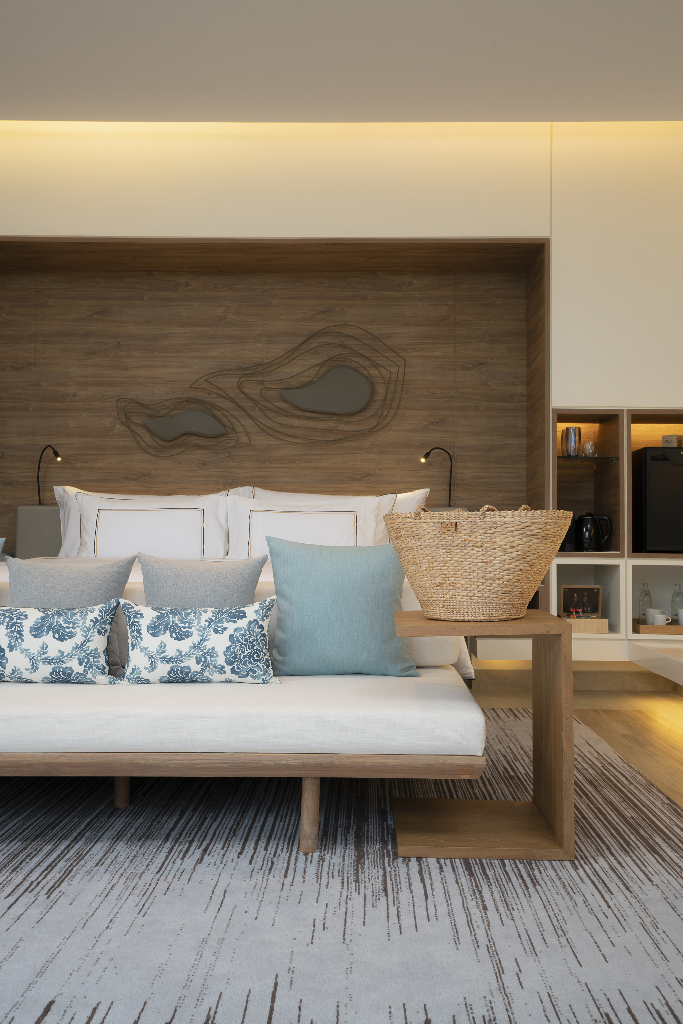 Modern resort room with bed, daybed, blue pillows, wood decor, woven bag.
